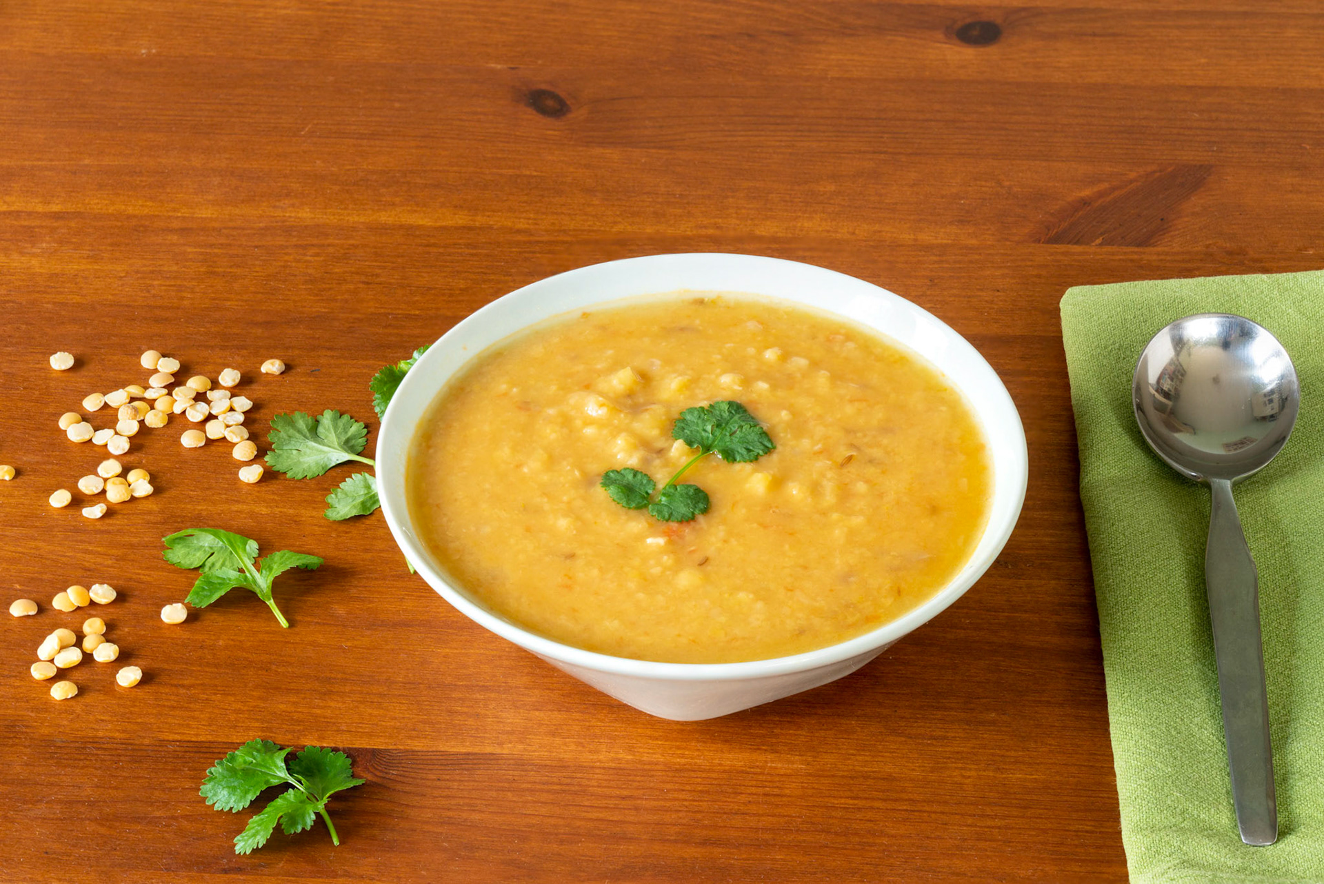 Yellow split peas lentil soup, garnished with corrinader leaves, in a bowl with a spoon and napkin on a wooden table. Copy space
