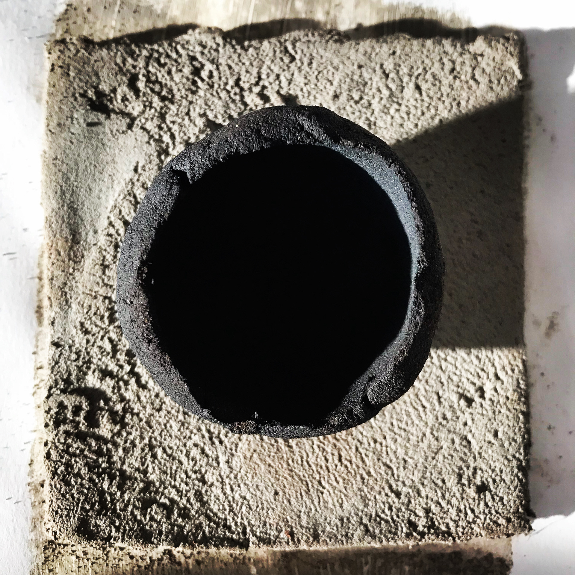 Beach clay pinch pot, tempered with sand, wood fired, straw reduction, placed upon unfired test tile of the same clay