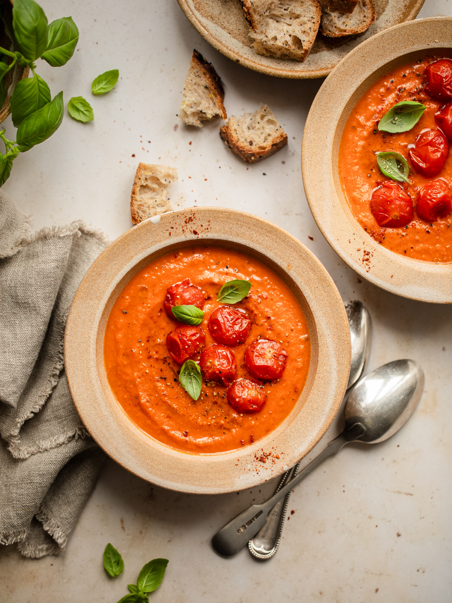 Image of tomato soup in bowls and served with bread, basil and topped with roasted tomatoes made and captured by Ioana Ursu Photographer and Food Stylist