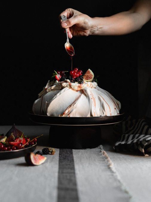 Image of Pavlova served with cream and fruit and a drizzle of strawberry sauce, served on a cake stand and accompanied by more fruit, made by Ioana Ursu - offering content creation, social media and sponsored posts services
