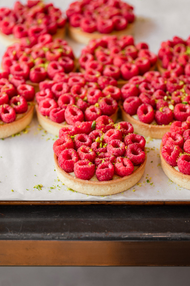 A hospitality image made for a local bakery presenting freshly made raspbery tarts with pistachios on a baking tray, made by Ioana Ursu food, restaurant and hospitality photographer based in Warwickshire
