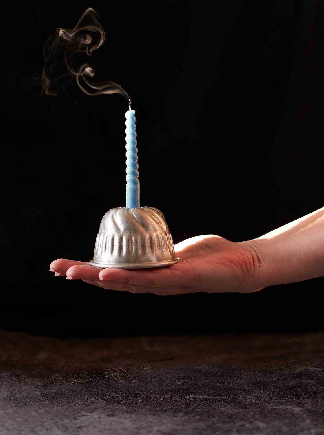 Käsi ojentaa kakkuvuokaa jossa kynttilä