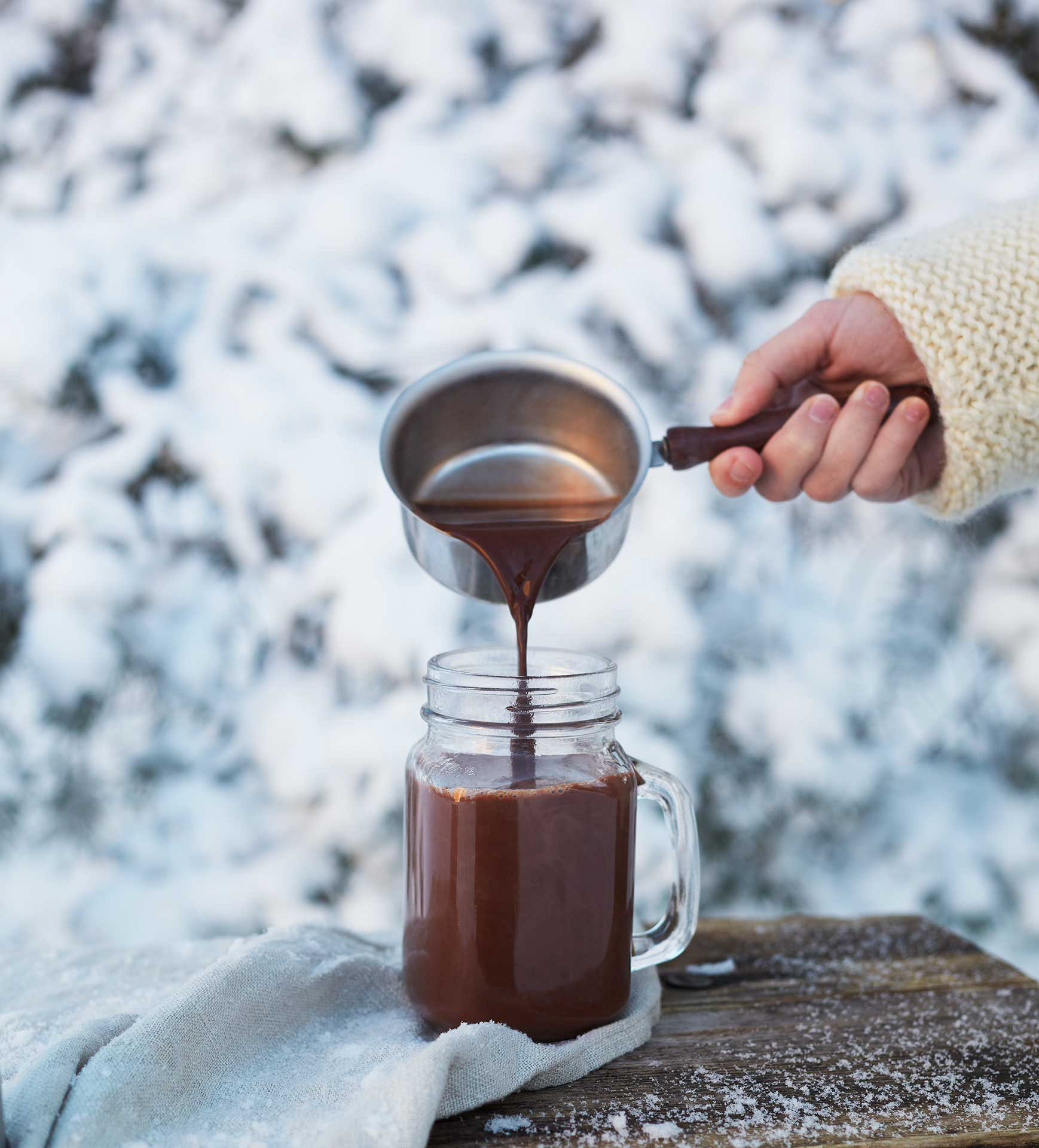 Käsi kaataa kaakaota mukin ulkona talvella