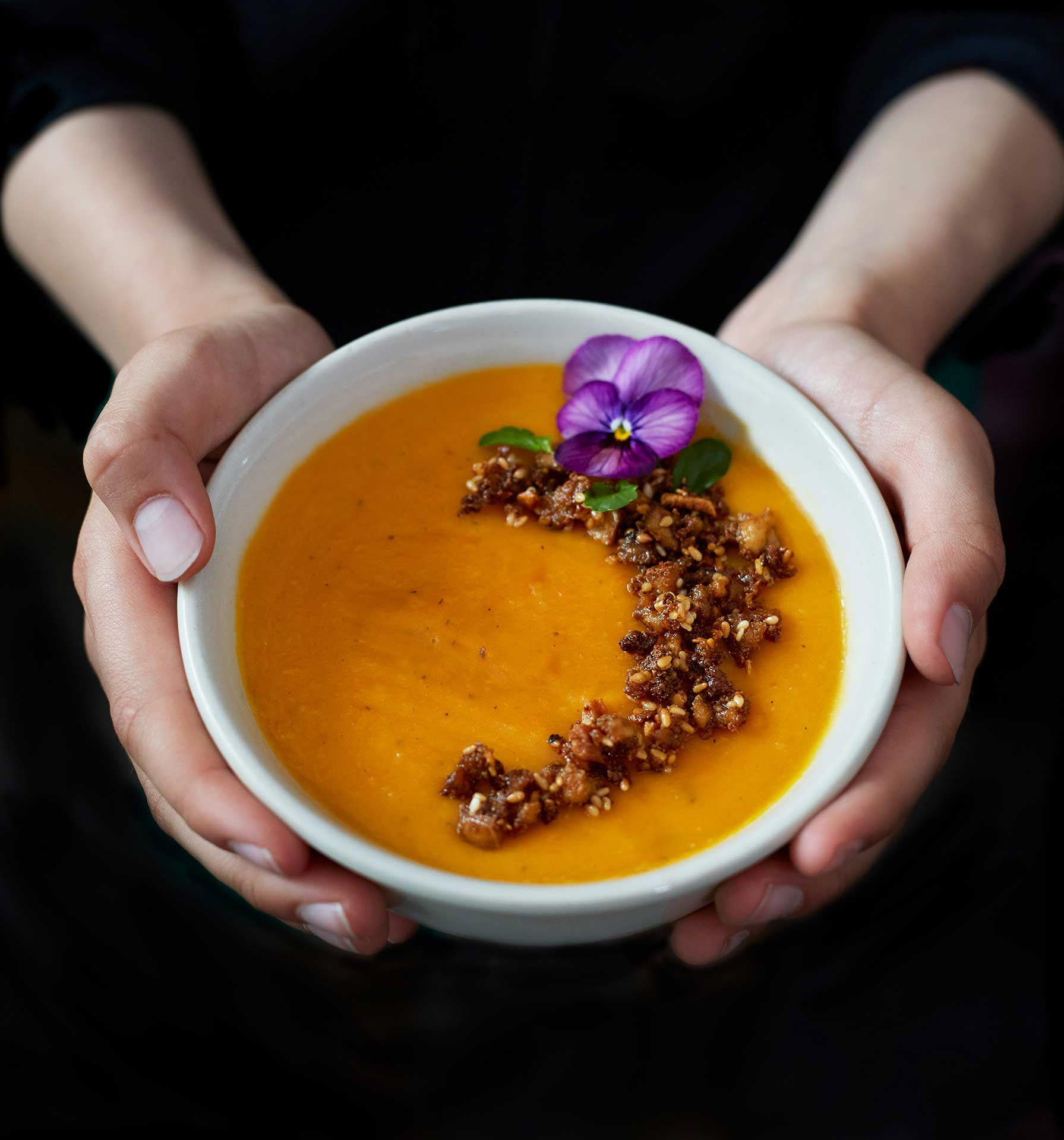 kädet ojentavat oranssia keittoa