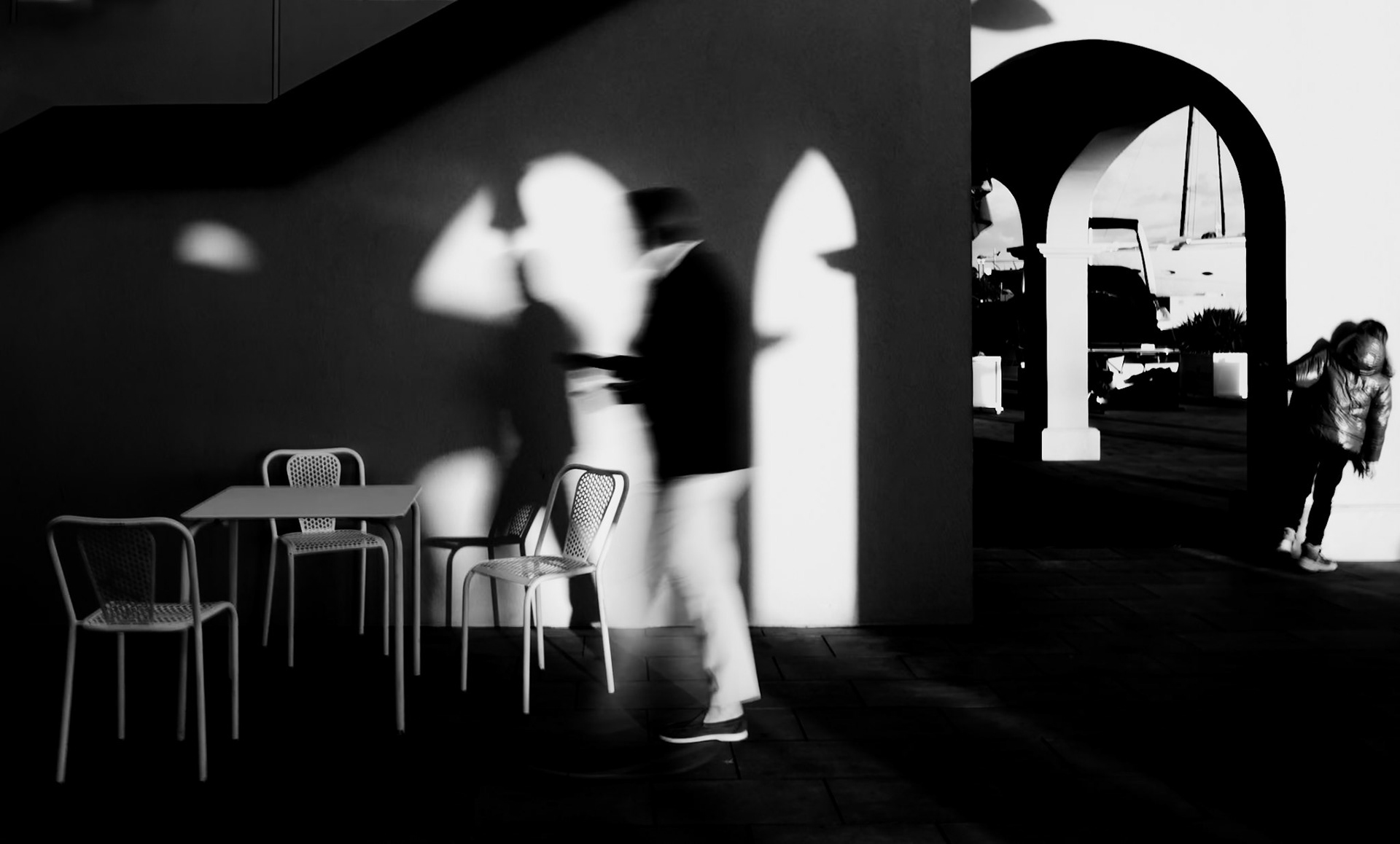 in this scene, the play of light and shadow creates a vivid tableau at a cafe terrace. blurred figures move through the golden glow of the evening, their outlines softened against the sharp silhouettes cast by the setting sun. it's a moment of daily life, wrapped in the warmth of sunset.