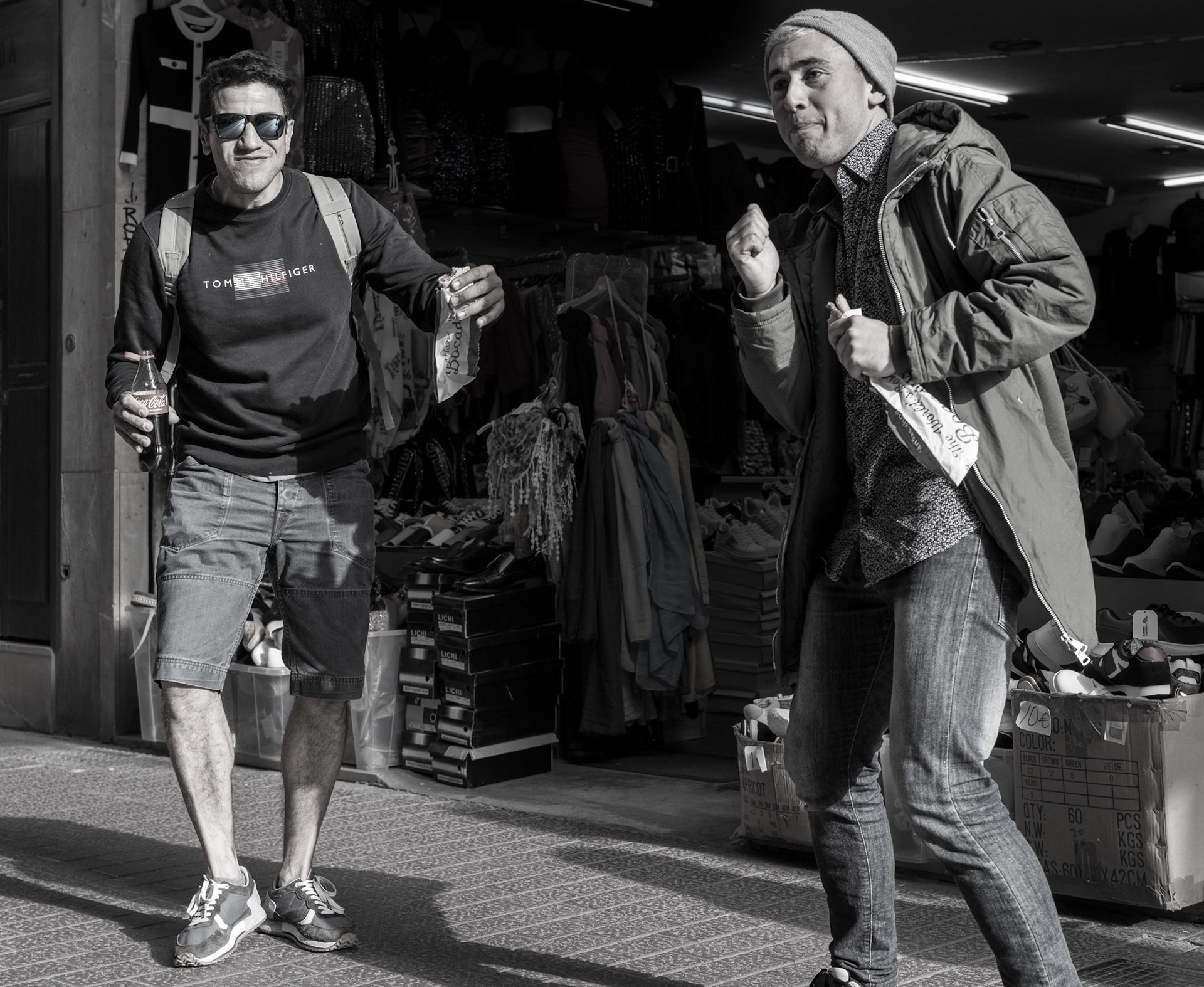 captured in the heart of palma's old town, this photograph encapsulates a moment of pure joy as two italians break into a spontaneous dance. the interplay of light and shadow highlights their movements and expressions, adding a dynamic energy to the scene. the background, filled with shops and mannequins, contrasts with the lively foreground, enhancing the sense of an unexpected burst of life in an ordinary setting. this image captures the essence of street photography, freezing a fleeting moment of happiness and human connection.