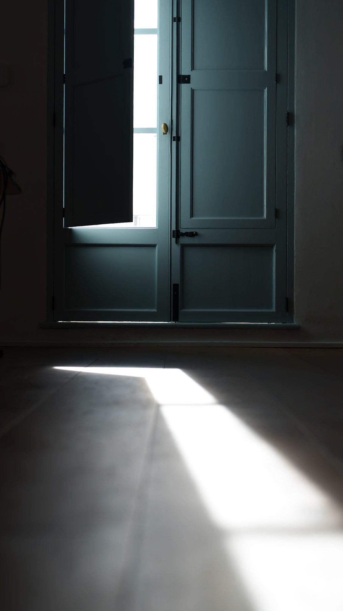 Capturing the quiet essence of our Portixol office, this photo highlights the old wooden door ajar, with sunlight streaming through to cast a sharp, geometric shadow on the floor, contrasting the darkness within and hinting at the world outside.