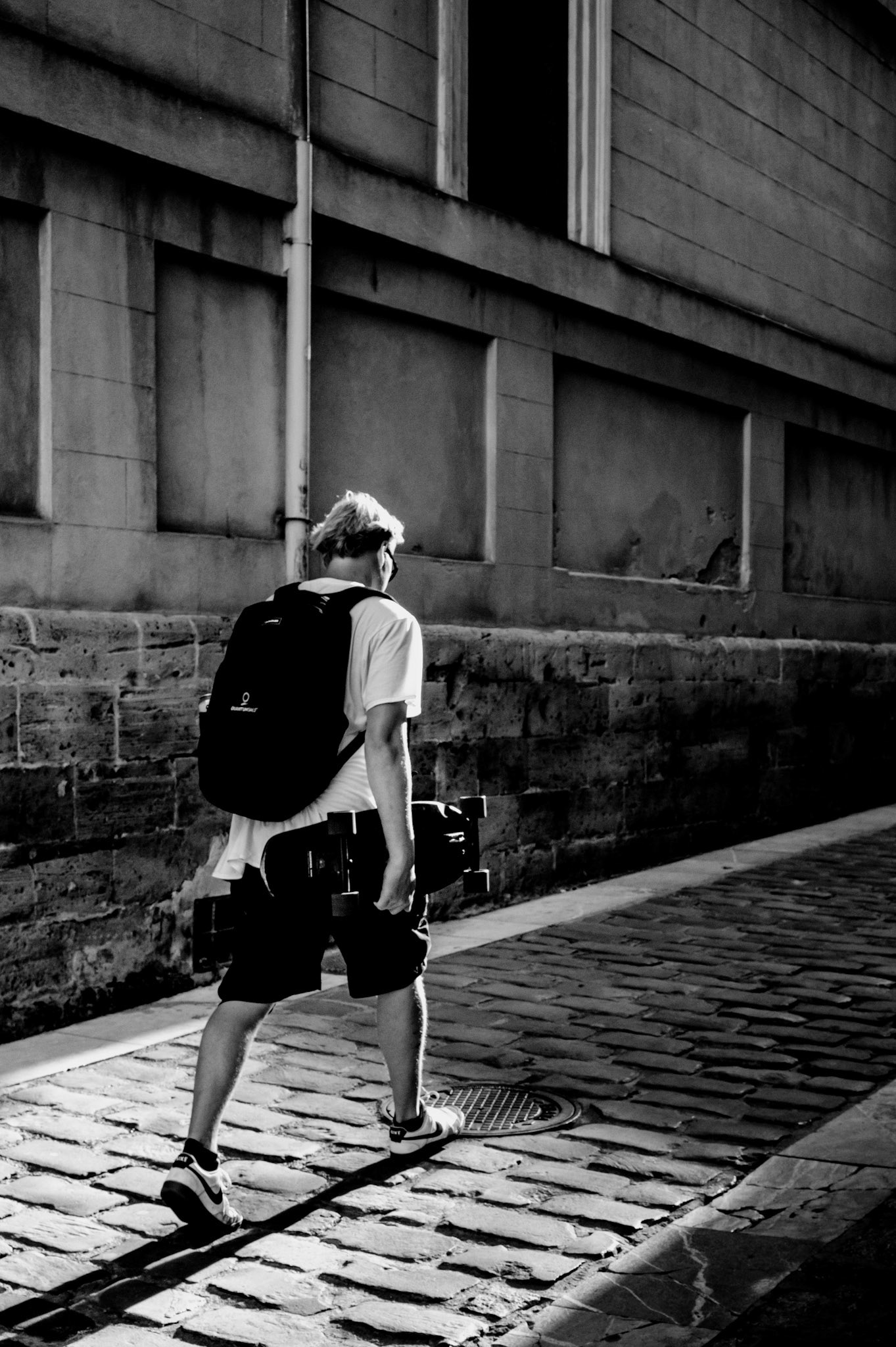 through the narrow alleys of calatrava, the skater walks with determination, his silhouette cast against the aged stone walls. the harsh sunlight creates a stark contrast, highlighting the textures and shadows of the ancient district. there’s a sense of quiet solitude in his stride, a quest for freedom amidst the confines of the city’s labyrinthine paths. the echo of his footsteps on the cobblestones speaks of resilience and a journey beyond the immediate, seeking a space where he can skate freely, unbounded by the urban restraints.
