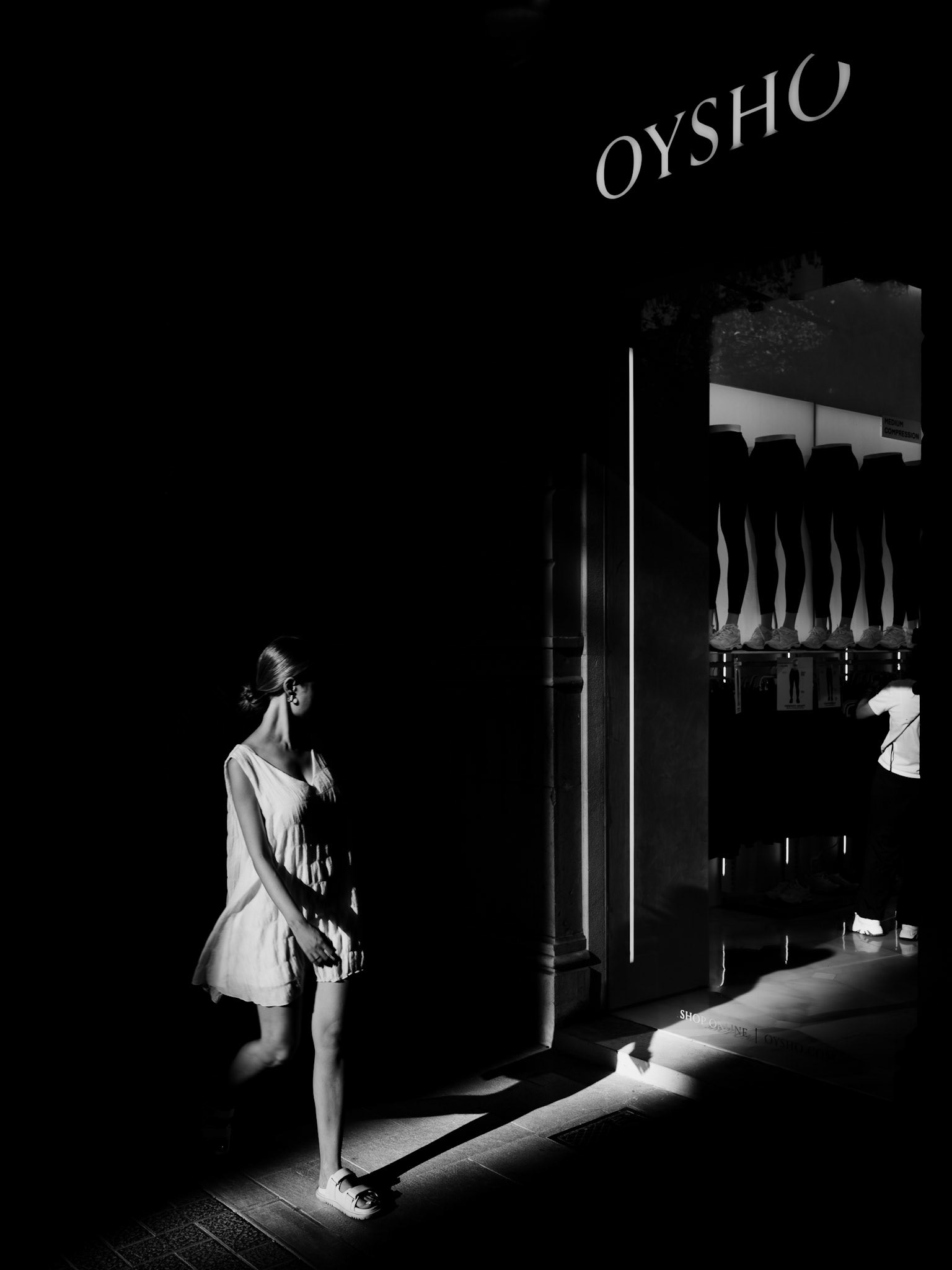 in the heart of palma's bustling paseo del borne, the interplay between light and shadow transforms the everyday into the extraordinary. captured here is a moment of ethereal beauty— a woman, wrapped in the delicate embrace of sunlight, stepping into a world where the darkness recedes just enough to reveal her presence. the minimalist aesthetic of the scene, with its stark contrasts, evokes a sense of quiet contemplation amidst the city's relentless pace. this is the magic of street photography—finding poetry in the most unexpected places, where light becomes the storyteller and shadows its ink.