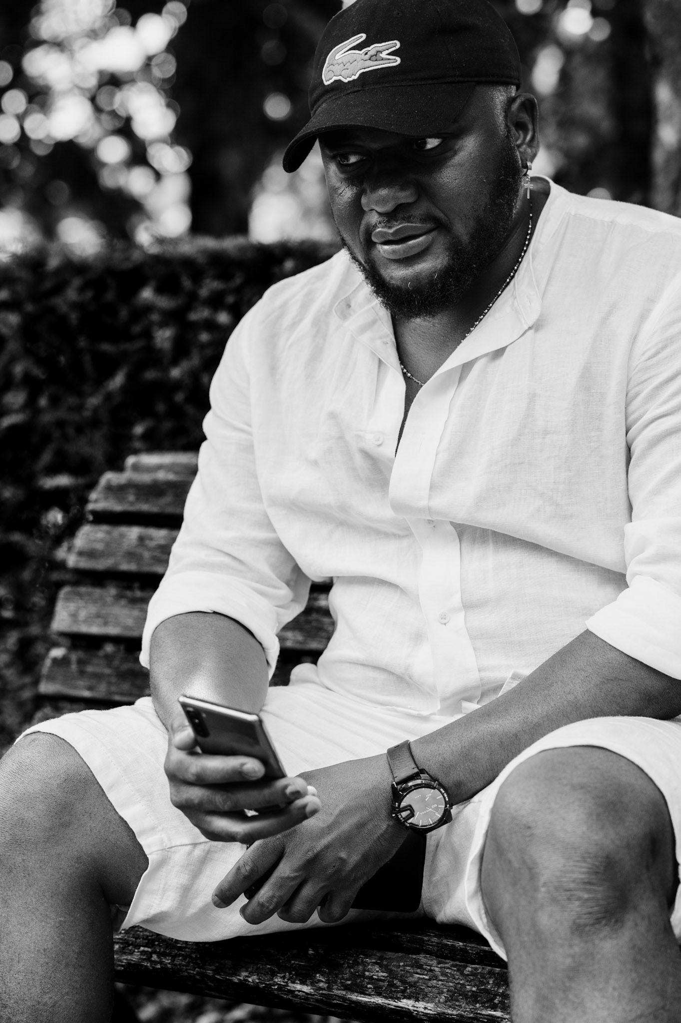 during a spontaneous walk in berlin's tiergarten, i captured this serene moment. a man sits on a weathered bench, engrossed in his thoughts while holding his phone. dressed in a light, casual outfit, his relaxed demeanor contrasts with the bustling city around him, reflecting a quiet moment of introspection and peace amidst the urban rush.