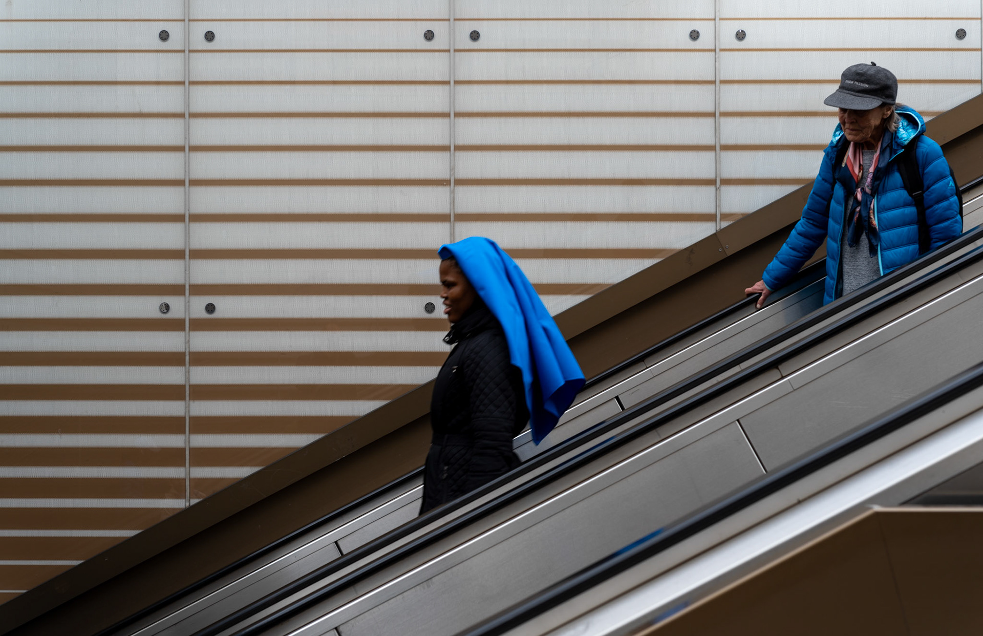 on the mechanical stairs leading into marienplatz's underground, lives intersect in fleeting ascent and descent. a vibrant blue scarf catches the eye, a splash of color against the muted tones of a daily commute. it's a juxtaposition of direction and purpose, each person a story, moving within the rhythmic heartbeat of the city. these stairs, a crossroads of sorts, a brief chapter in countless narratives that weave through the heart of munich.