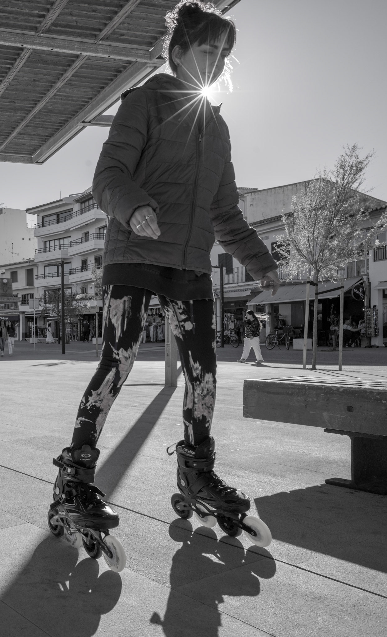 late afternoon in port de pollenca, the sun plays hide and seek with the silhouettes. a figure, poised on wheels, carves the light into a starburst that crowns her – a momentary coronation. shadows stretch long and lean like the tales of summer, whispering along the concrete canvas. in this dance of light and shadow, every turn is a brush stroke, every glide is a word in a story told by wheels that never tire. she's caught in a chiaroscuro reverie, where even the sun can't help but pause in its skyward climb to watch.