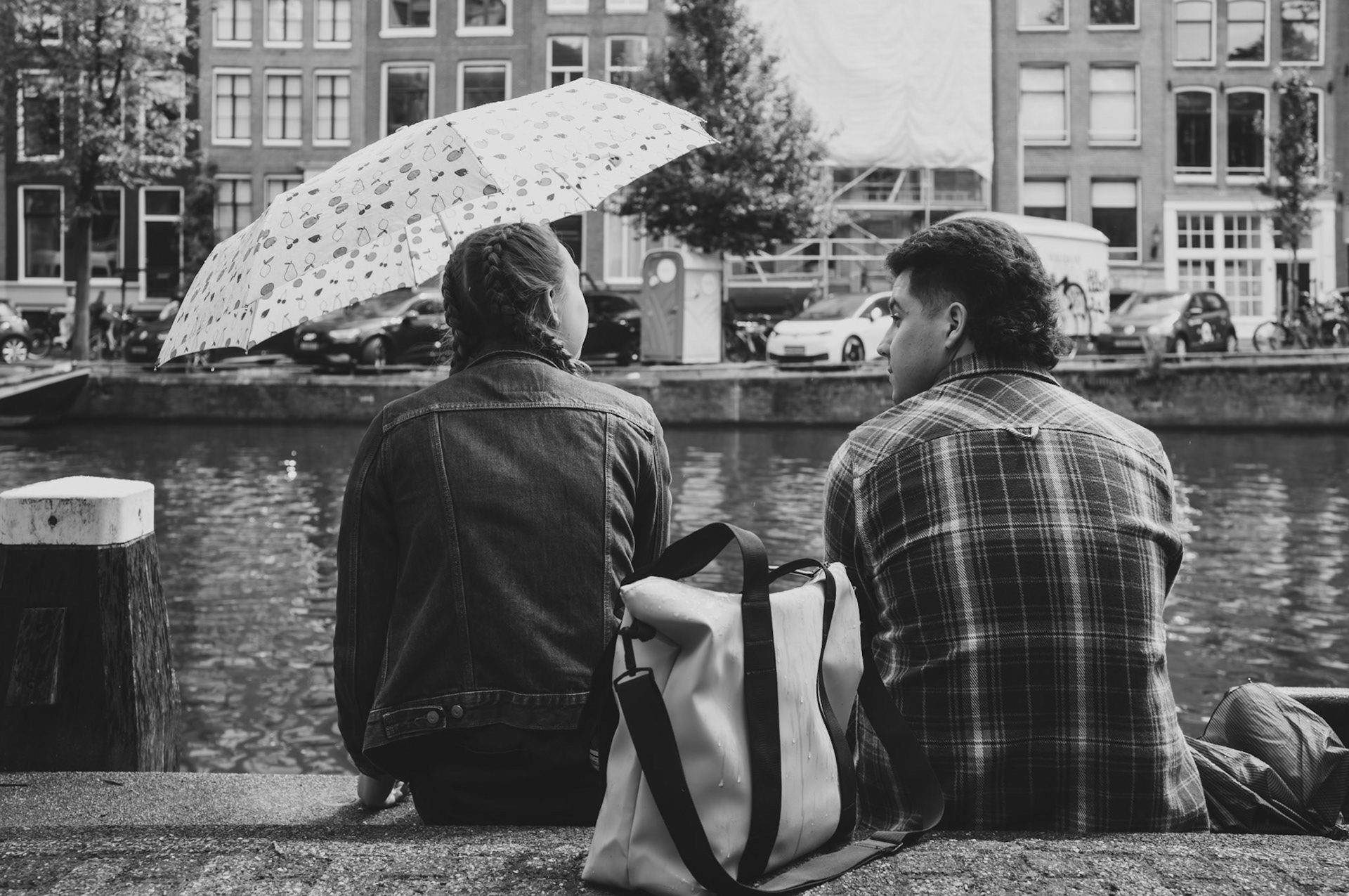 under the soft drizzle of an amsterdam day, two sit close yet worlds apart. the umbrella, a shield against the rain, seems to represent the quiet thoughts each keeps hidden. a scene of quiet connection, where even in shared space, individual worlds remain distinct.