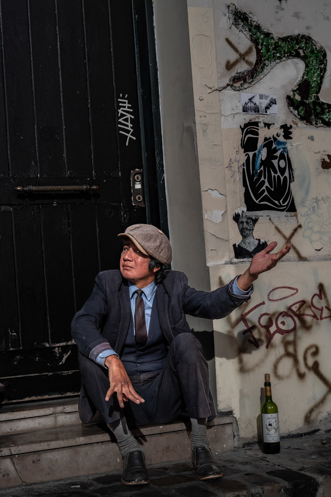 in the heart of montmartre, where art and the streets blend seamlessly, a man sits on steps, his attire weathered yet full of character. a bottle of wine rests beside him, as if it carries the stories of the street within. his hands gesture towards the sky, telling tales only the city could inspire. behind him, graffiti and street art mirror the vibrant pulse of paris, casting a contrast between tradition and rebellion. bathed in dramatic light and shadows, this moment feels cinematic, capturing the essence of montmartre—a neighborhood rich in history, creativity, and untold stories.