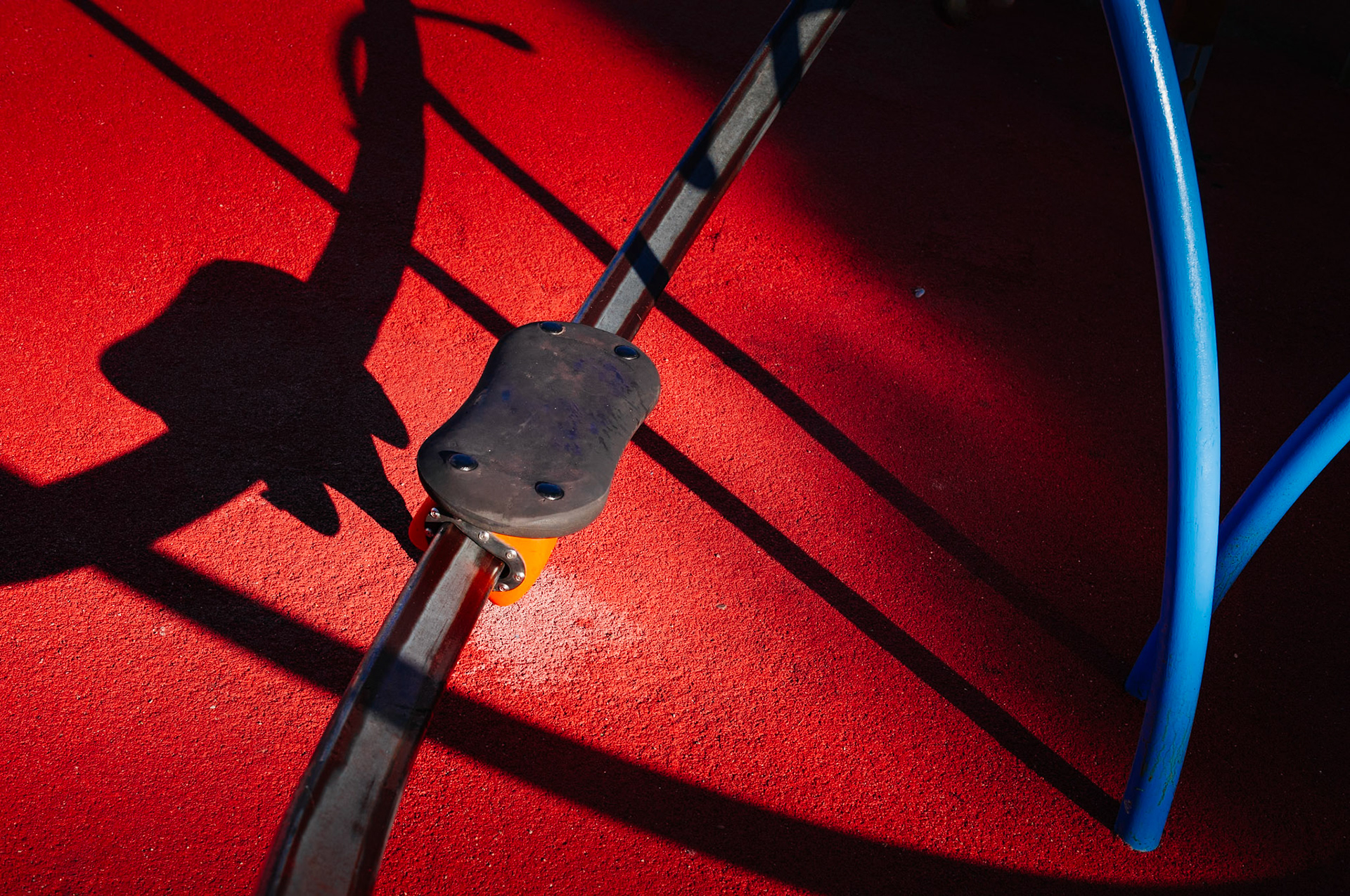 captured in palmanova, this photo is part of "a morning at the playground" series. the winter sun casts long shadows, creating a stark contrast against the vibrant red safety surface. the playground stands quiet, its colorful spring rider poised in stillness, waiting for the laughter and chaos of play that comes with the warmer days.