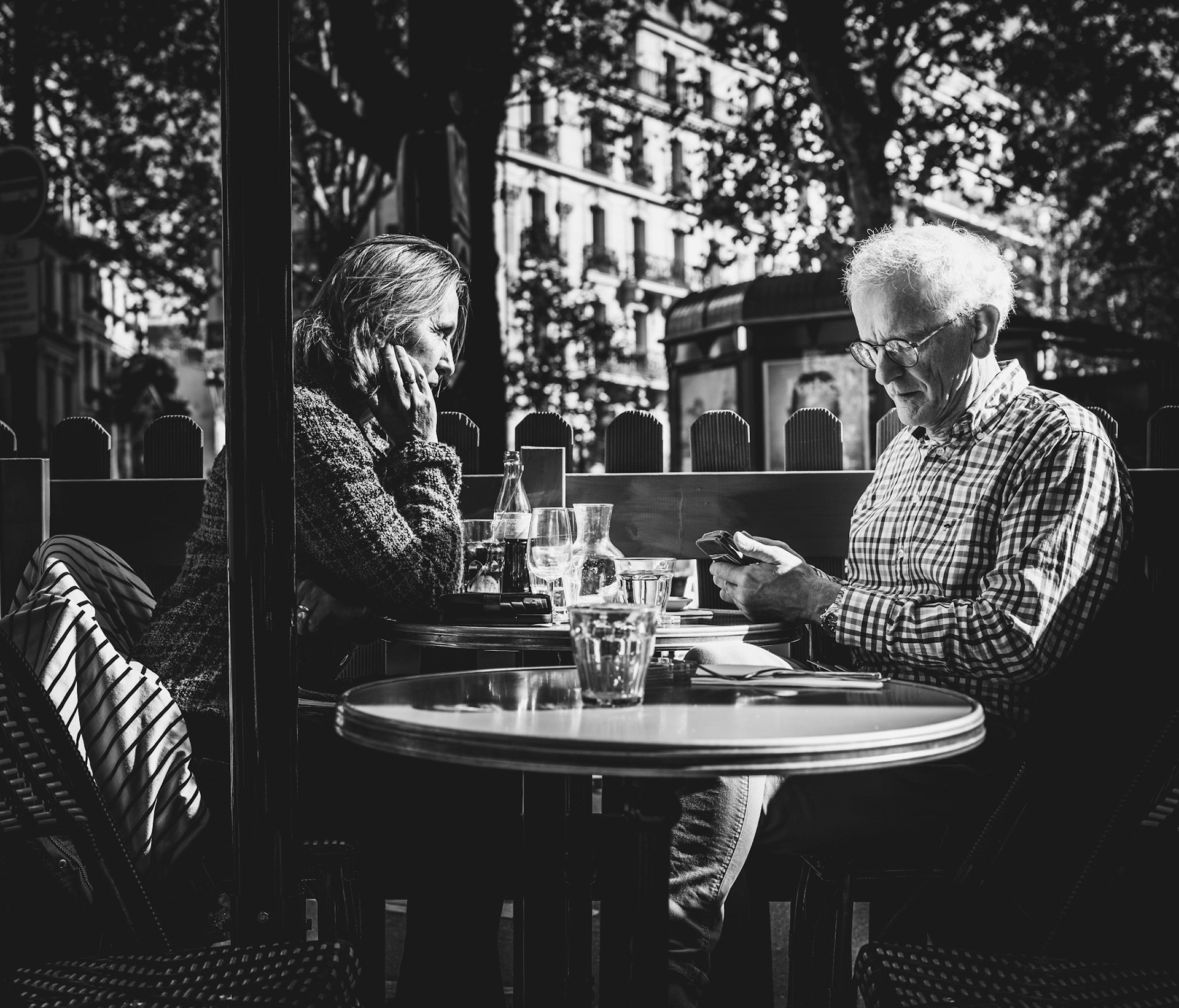 captured at a paris café, this image speaks to the quiet, introspective side of city life. amidst the afternoon bustle, these two figures share a table but remain in separate worlds, each lost in thought. the play of light and shadow, reflections on the glassware, and the subtle details of their expressions capture a timeless parisian moment—one of quiet presence and understated connection. it’s a glimpse into the beauty of everyday solitude in the heart of the city.