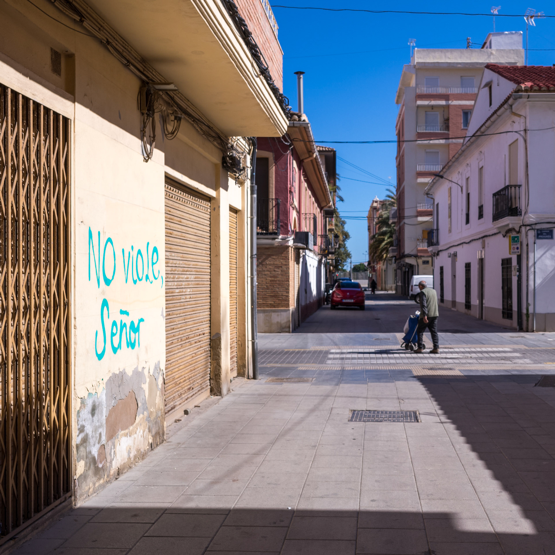 against the vibrant backdrop of cabanyal, where the pulse of valencia meets the calm of the sea, stands a stark blue declaration, "NO viole, Señor" — a cry against the violation of sanctity, a graffiti artist's plea for respect on the canvas of the city's skin. it's a poignant reminder on this international women's day, resonating with the global call for an end to violence against women. a solitary figure maneuvers the street, perhaps oblivious, perhaps painfully aware, of the weight the words carry. shadows carve the scene, a play of light and life, of silent stories that scream to be heard, a juxtaposition of daily life against a backdrop of communal defiance.