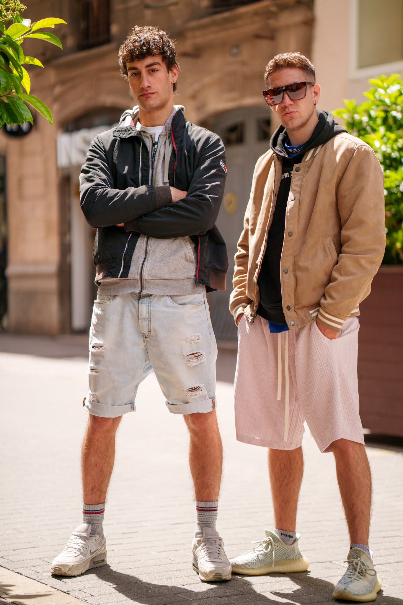 in the beating heart of palma, a stone's throw from the bustling mercat de l’olivar, two young italians step into the frame with ease. they carry the casual confidence of the youth, a nonchalance that's almost palpable as the sun spills over the cobblestone. one stands arms crossed, the other with hands tucked nonchalantly into his pockets, both faces partially masked by the shadows of their own creation. the city breathes around them, a symphony of midday murmurs and the distant laughter of a place unbothered by the ticking clock. they are, in this moment, the unscripted ambassadors of street style, their fashion a blend of purpose and spontaneity, just like the city they find themselves in.