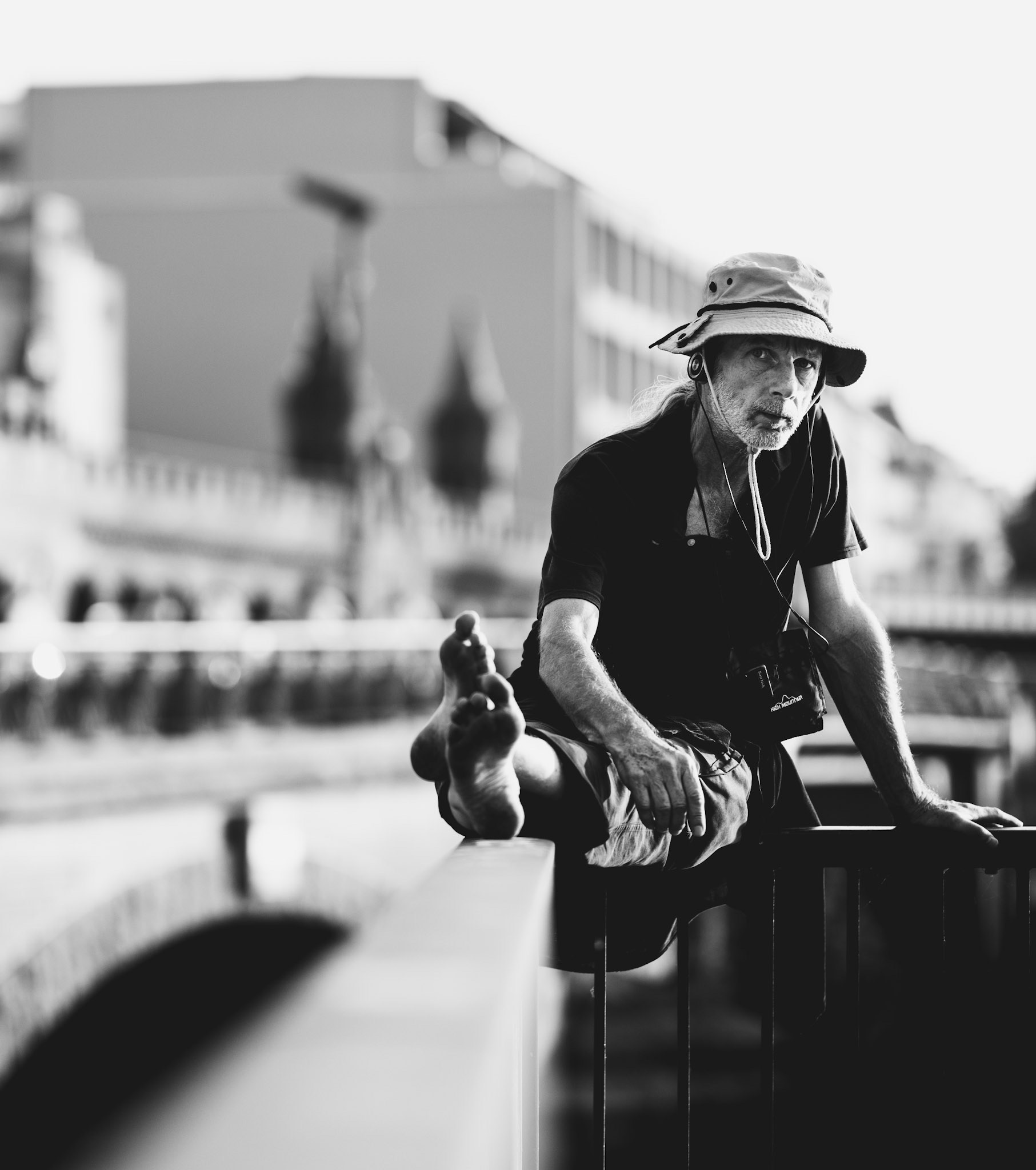 as the sun dips low behind berlin’s skyline, a quiet moment lingers. the iconic arches of oberbaumbrücke stand tall, a backdrop to a figure suspended in thought, half-perched, half-leaning. bare feet trace the metal rail, while earbuds whisper solitude into his ears. the gritty urban essence mixes with a sense of freedom, evoking questions of what lies beyond. this is berlin: a city of contrasts, where reflections become part of the journey, and the streets carry whispers of stories untold.