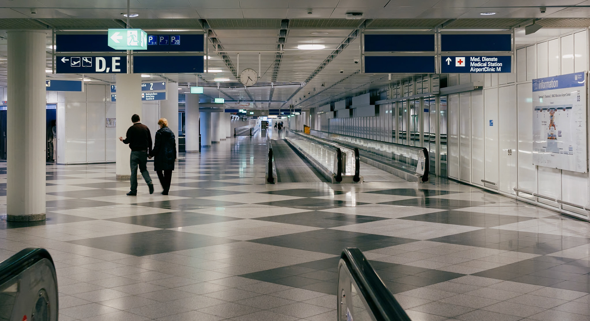 at munich's gateway to the world, the airport thrums with a quiet rhythm in the off-hours. amidst the sprawling, pristine halls, there's a warmth to the scene—a couple, hands intertwined, walking together. they move through the clinical precision of the departure lounge, a human touch in stark contrast to the cold geometry of tiles and the mechanical glide of walkways. their closeness whispers a narrative of shared journeys, a personal story unfolding silently in the vast, impersonal transit space. it's a moment of connection, a small narrative of togetherness, in the grand theatre of travel.