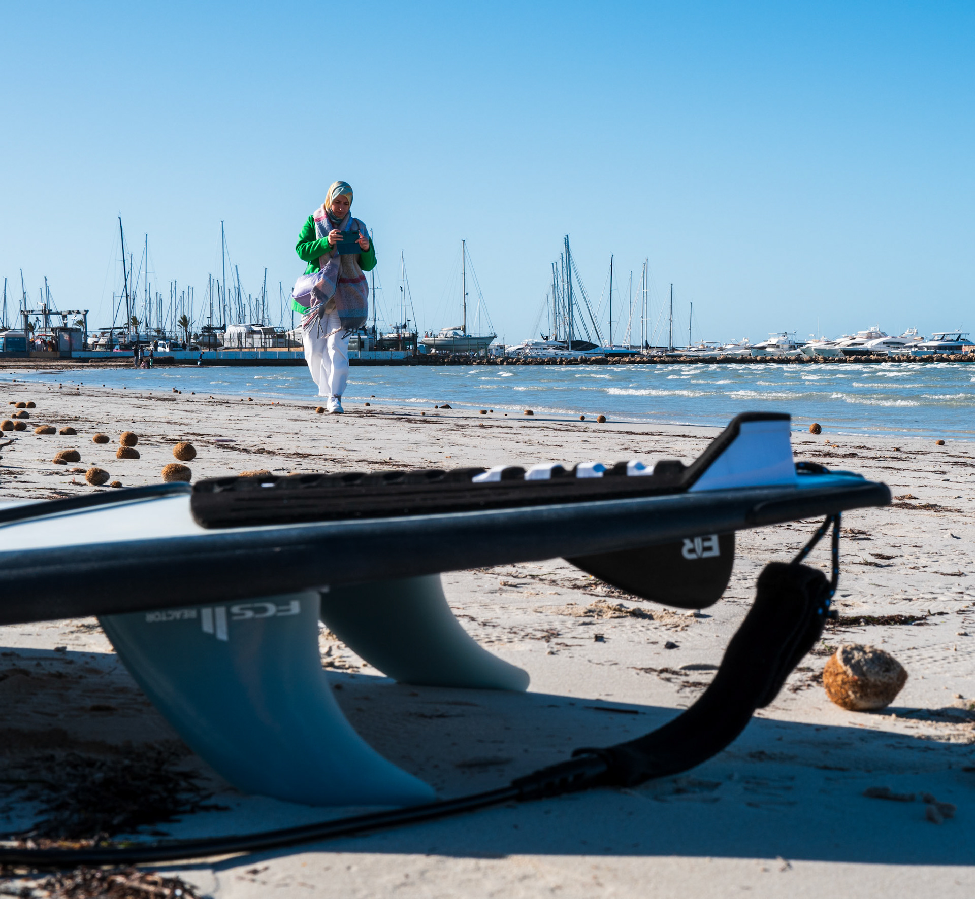 in el arenal's winter, the beach transforms. it sheds the summer crowd for a quiet, more introspective scene. a lone surfboard rests on the sand, foregrounding the bustling marina. the boats seem to slumber in the low season's peace. the sun still bathes the landscape in warmth, but it's the adventurous spirit of the few who wander or paddle out that keeps the spirit of summer alive. amidst the tranquility, one can almost hear the soft whispers of the sea calling out to those looking for solace on its shores.