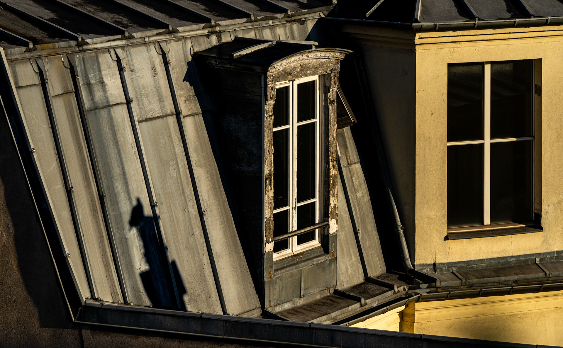 captured from our hotel room as dawn breaks over the rooftops of paris, this image tells a story of quiet charm and age-old character. the soft morning light touches worn wood frames and the weathered metal of an old parisian window, casting a shadow of a streetlamp like a silent sentinel across the roof. each detail, from the faded texture to the gentle edges, seems to hold a secret, an echo of artists who once wandered these streets, inspired by the same view. this is a still tribute to the history and poetry lingering in the rooftops of montmartre.