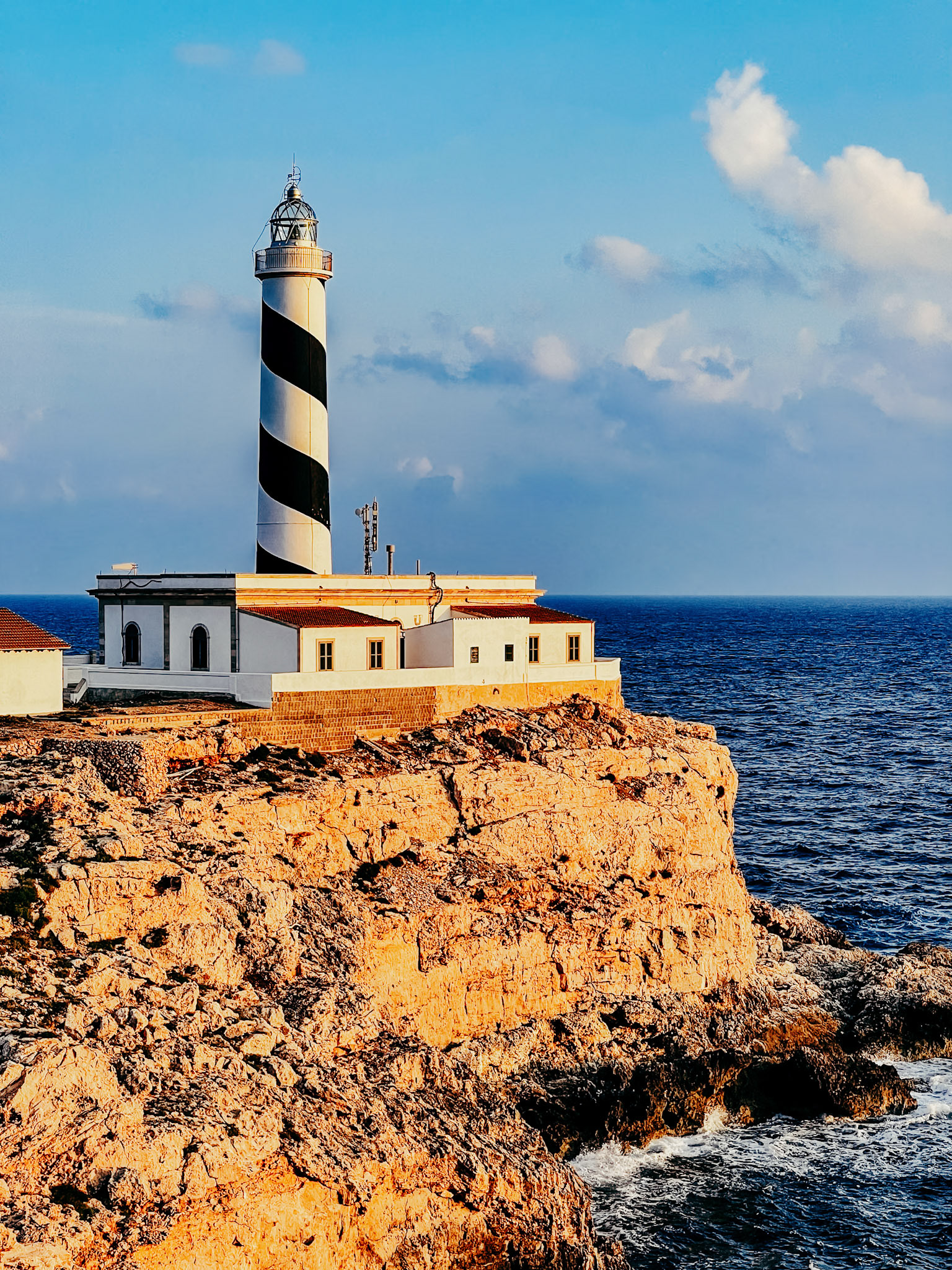 perched on the rugged cliffs of cala figuera, mallorca, the lighthouse stands as a timeless sentinel. its stripes are a beacon of guidance, slicing through the blend of blue sea and sky. this structure, both stoic and elegant, watches over the waves that have crashed against these rocks for centuries. at the golden hour, the sun casts a warm glow over the stone, transforming the lighthouse into a symbol of the island's enduring spirit, its light a whisper to seafarers of safety and home.