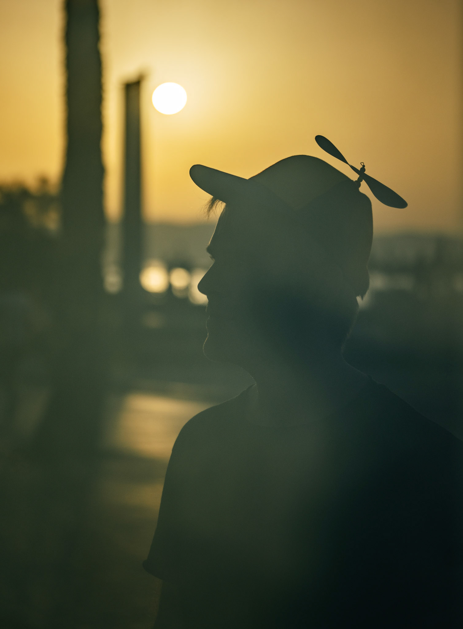 during a late afternoon photowalk in el arenal, my friend thomas, a street photographer with a penchant for close, frontal shots, donned a whimsical propeller cap to blend into the vibrant environment. using his Ricoh GR3, he captured the essence of urban life from an intimate perspective. this photo, however, captures thomas himself, reflecting through a plexiglass panel, bathed in the golden hues of the setting sun. the playful propeller on his cap adds a touch of humor and lightness to the scene, perfectly embodying his approach to photography.