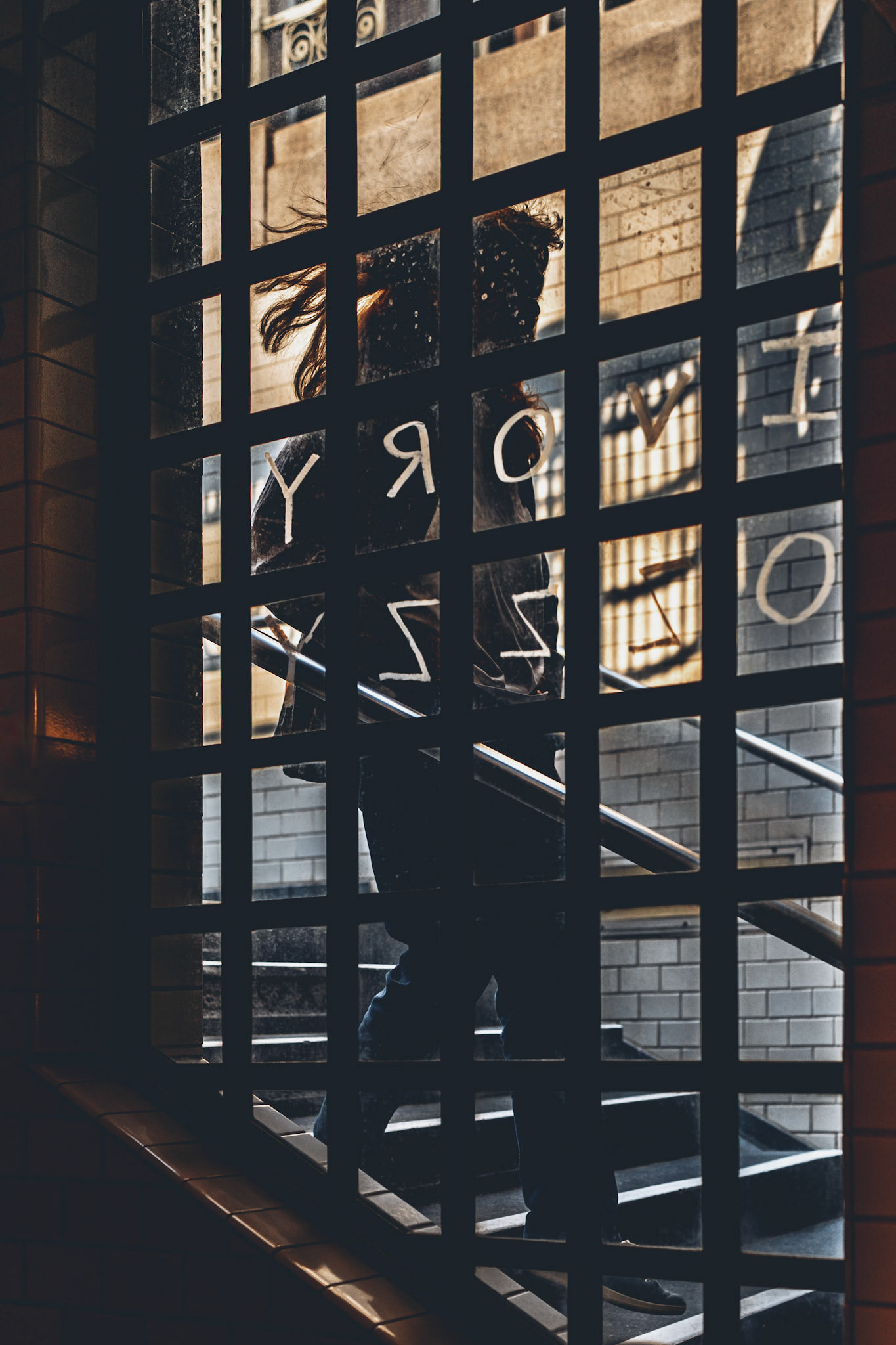 in the stillness of the underground, shadows tangle with streaks of sunlight as they crawl across the stairwell. a figure ascends, caught between grids of light and darkness, like a prisoner of time itself. every step echoes, every ray of light a reminder of the world above. yet, it’s the fleeting moment—just before crossing into the daylight—that holds the weight of stories untold.