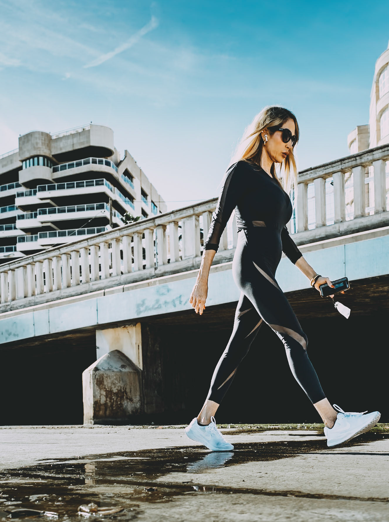 captured in palmas paseo maritimo, this photograph showcases a woman confidently striding along a pathway with modern buildings in the background. her athletic wear and focused demeanor suggest a moment of personal dedication and purpose, set against the striking architecture that frames the scene. the bright, clear sky adds a vibrant contrast to the urban elements, enhancing the overall composition. this image captures a moment of contemporary life, blending personal fitness with the bustling rhythm of the city.