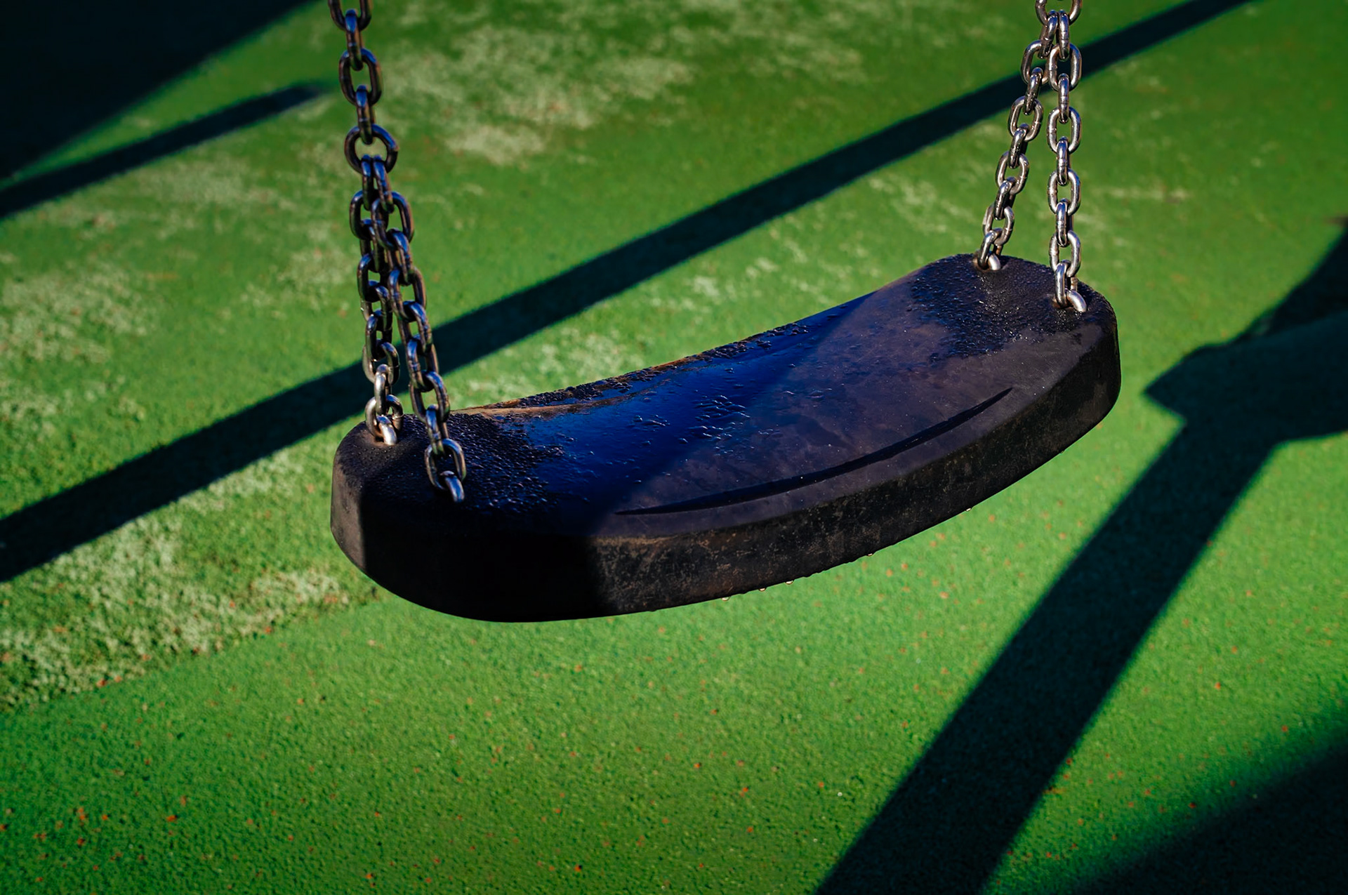 captured in palmanova, this photo is part of "a morning at the playground" series. the winter sun casts long shadows, creating a stark contrast against the vibrant red safety surface. the playground stands quiet, its colorful spring rider poised in stillness, waiting for the laughter and chaos of play that comes with the warmer days.