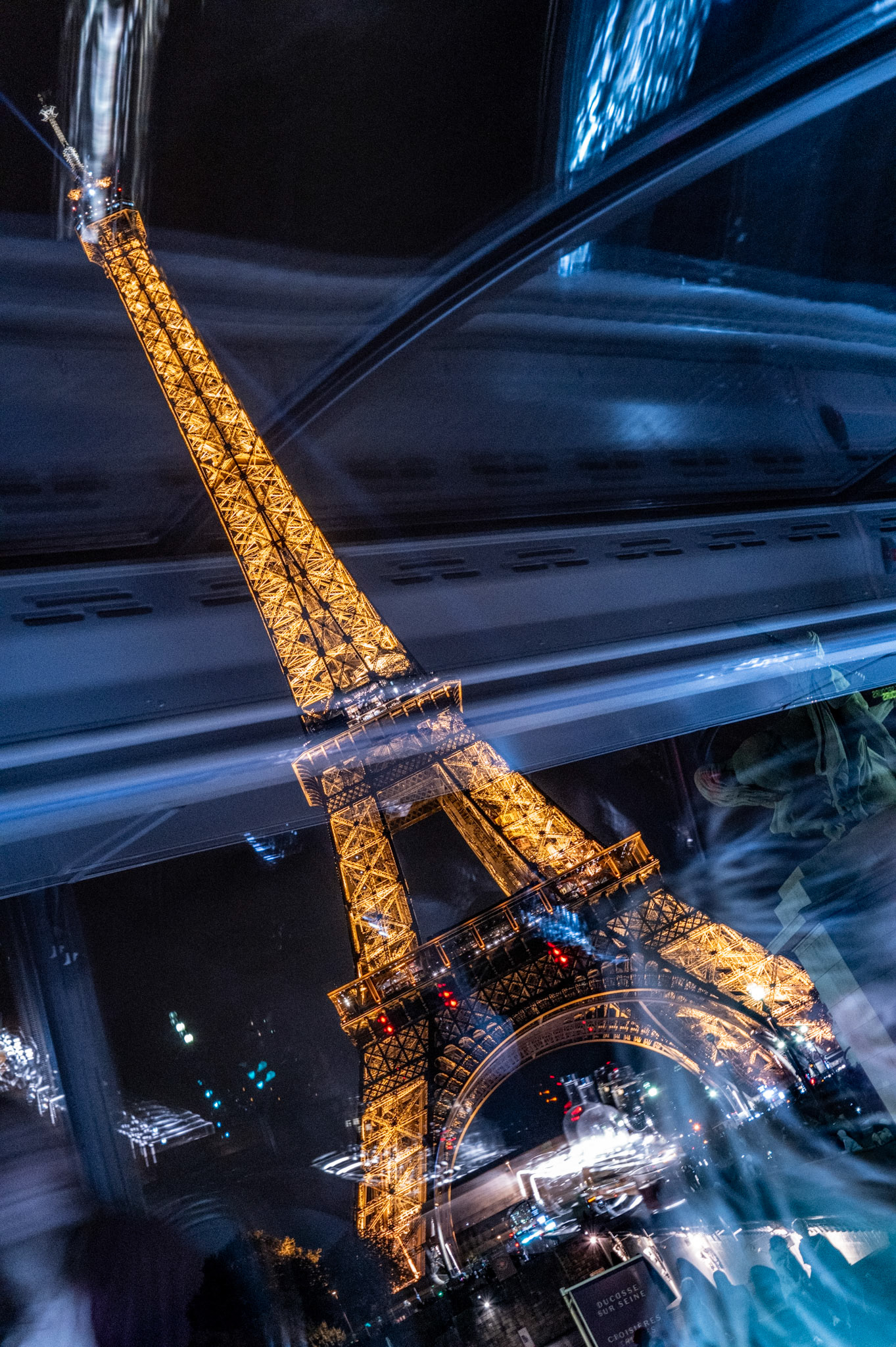 this photo presents an abstract interpretation of a classic tourist icon—the eiffel tower—captured at night in a unique, reflective twist. the vibrant golden lights of the tower are mirrored and blurred by the surfaces of nearby glass, creating a surreal dance between shadow and brilliance. this nighttime view transforms the monument into a dynamic piece of art, a departure from its static daytime presence, inviting viewers to see beyond the ordinary.