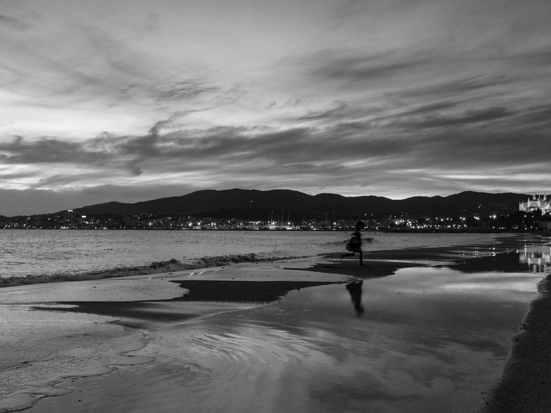captured on a chilly winter evening at the playa de palma, this image brings forth a serene and almost melancholic atmosphere. the blur of a figure running along the shore contrasts against the stillness of the water, reflecting the dimming light of the setting sun. distant city lights flicker like stars on the horizon, mirroring the calm before the night fully sets in. this photograph speaks of quiet moments and the gentle embrace of solitude by the sea.