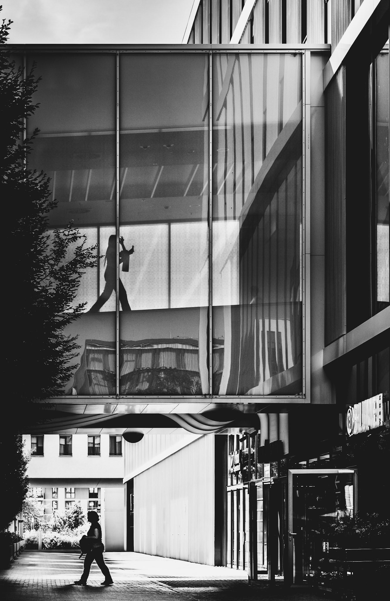 captured at the riem arcaden in munich, this shot encapsulates the interplay between architecture and human movement. the striking geometry of the glass bridge, combined with the silhouettes of the figures, creates a scene that feels both structured and fleeting. reflections in the glass and the sharp contrasts of light and shadow add layers of depth, making the viewer pause to consider the unseen stories of those crossing paths. it’s a moment that embodies the rhythm of city life—where every movement is framed within the urban canvas.
