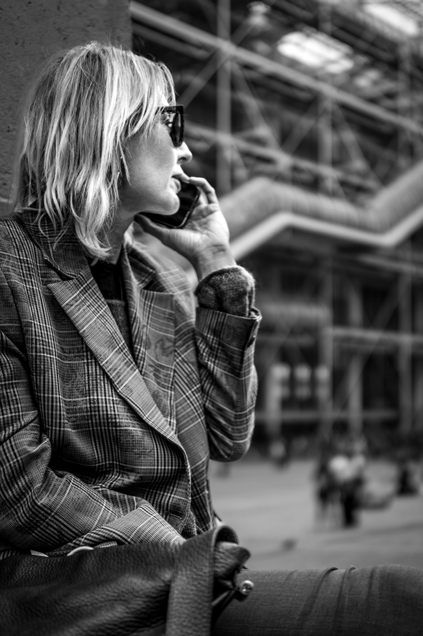 the subject sits amidst the industrial heart of paris, caught in a private moment of conversation, her thoughts flowing like the urban energy around her. the geometric patterns of the centre pompidou blur behind her, hinting at the constant motion and life that surrounds her, but in this frame, time seems paused. her expression, calm yet introspective, offers a window into the stillness we all seek, even when immersed in the city's hum. the contrast between the sharp lines of her attire and the soft blur of the background plays into the delicate balance of personal moments in public spaces, where noise meets quiet, and the individual remains alone in thought.
