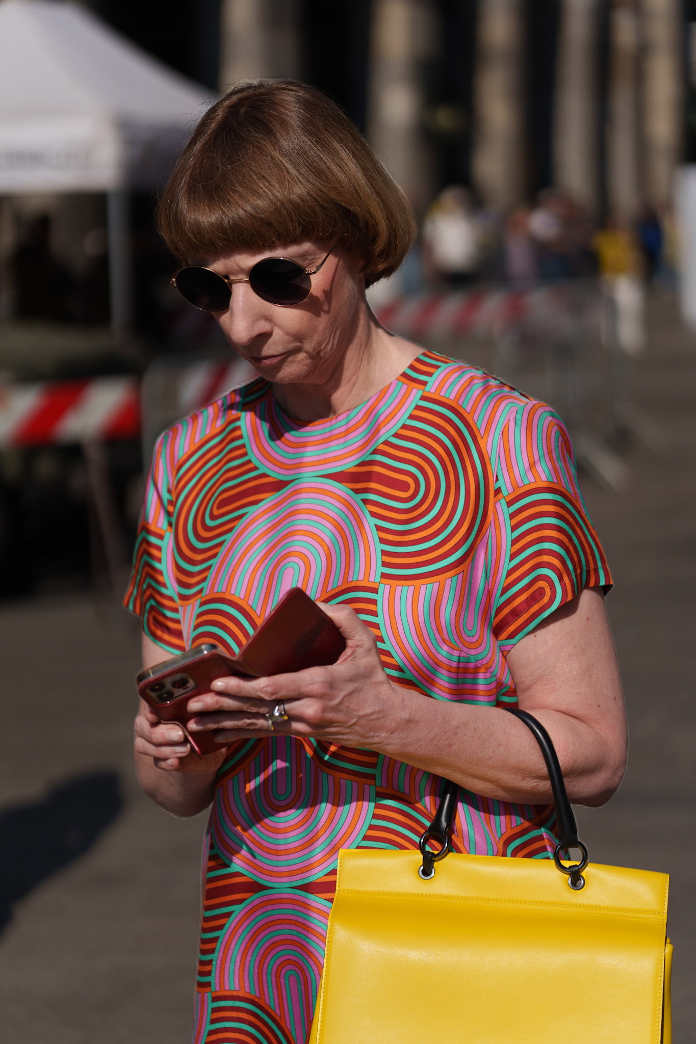 just a stone's throw from the piazza del duomo in milan, the weekend morning light casts a gentle glow on a passerby. wrapped in a dress of vibrant swirls that echo the lively spirit of the city, she pairs it effortlessly with a bold, sun-yellow tote. her gaze, fixed on the phone in hand, is a modern connection woven into the tapestry of a historic sunday morning. amidst the grandeur of milan’s architectural treasures, life unfolds in the simple act of reading a message, a quiet contrast to the vast stories etched in the stone of the cathedral nearby.