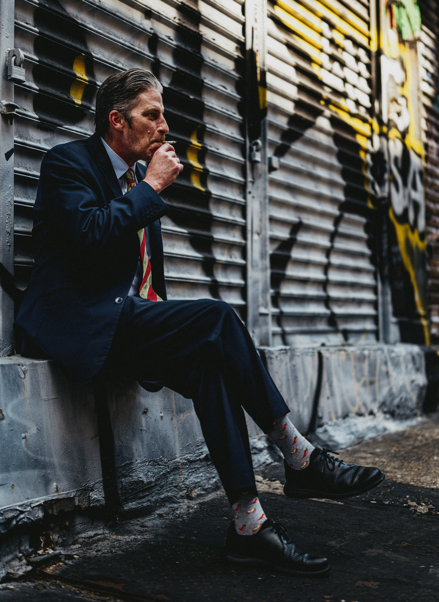 on a morning in soho, along crosby street, the concierge of the crosby street hotel savors a cigarette. the juxtaposition of his polished suit against the gritty, graffiti-covered backdrop captures the essence of urban life – a blend of sophistication and raw, street-level reality. his colorful socks add a touch of whimsy to the scene, underscoring the individuality and small rebellions that thrive in the heart of the city.