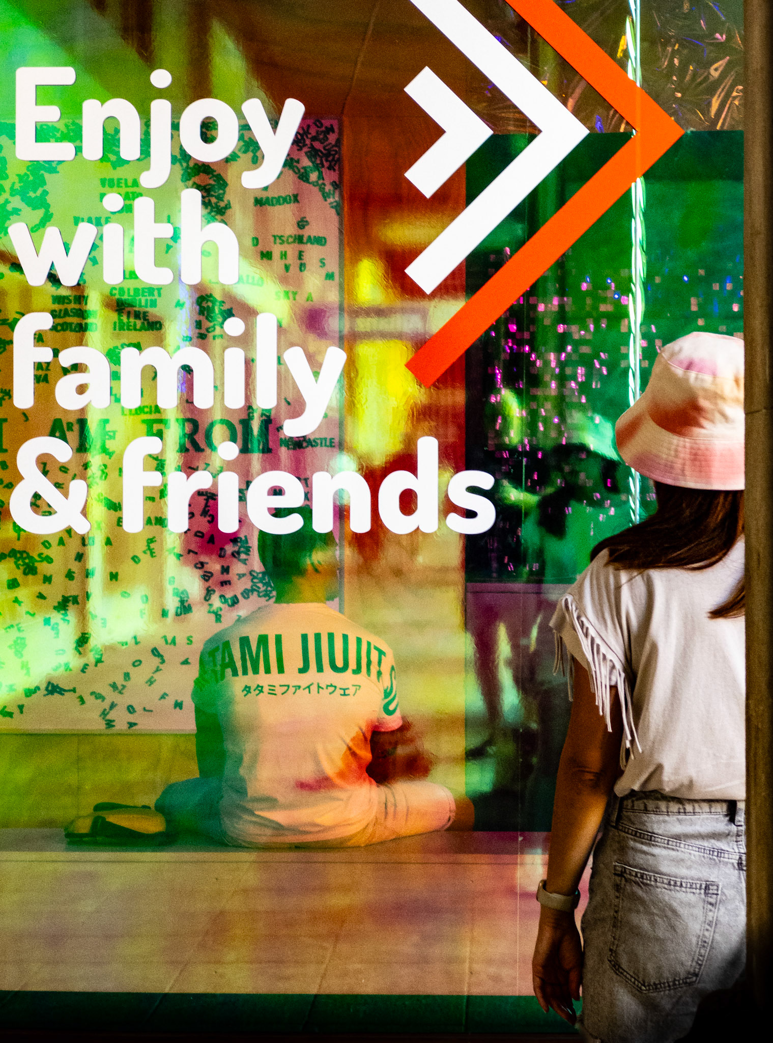 captured at plaça major in palma, this photo blurs the lines between reality and reflection, merging vibrant colors with everyday moments. the text on the glass, "enjoy with family &amp; friends," contrasts with the figures behind, creating a layered narrative of togetherness and observation. it’s a visual dance of light, color, and context—a playful reminder of how we see and interpret the world around us.