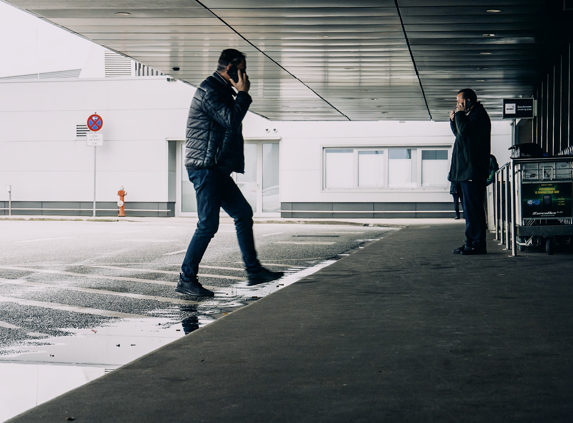 on a brisk winter day at hannover airport, life unfolds in a symphony of movement and pause. one man strides purposefully, phone pressed to his ear, caught in the swift current of travel. nearby, another stands still, savoring a cigarette, a solitary figure against the backdrop of an airport in constant motion. their parallel stories—a vivid portrayal of modern transit—reflect the contrasting rhythms of life's journey.