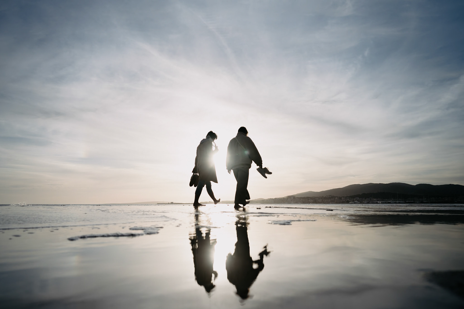 as the sun casts its last golden rays over the city beach of palma, a couple's silhouette is etched against the winter's evening sky. their reflections on the wet sand are as fleeting as the day's final moments. together, they walk in harmony with the sea's gentle rhythm, their presence a silent testament to the day's end and the quiet intimacy shared in this serene setting. it's a moment where time pauses, allowing them to savor the beauty of the mediterranean twilight.