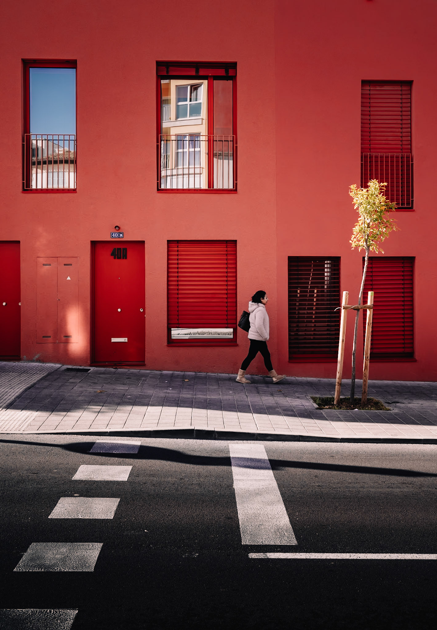 in el terreno, a district teeming with life in palma de mallorca, stands a striking red building, a creation of gras arquitectos. bathed in the soft morning light, its bold color contrasts beautifully against the crisp shadows. a lone figure walks by, adding life to the serene, architecturally balanced scene.