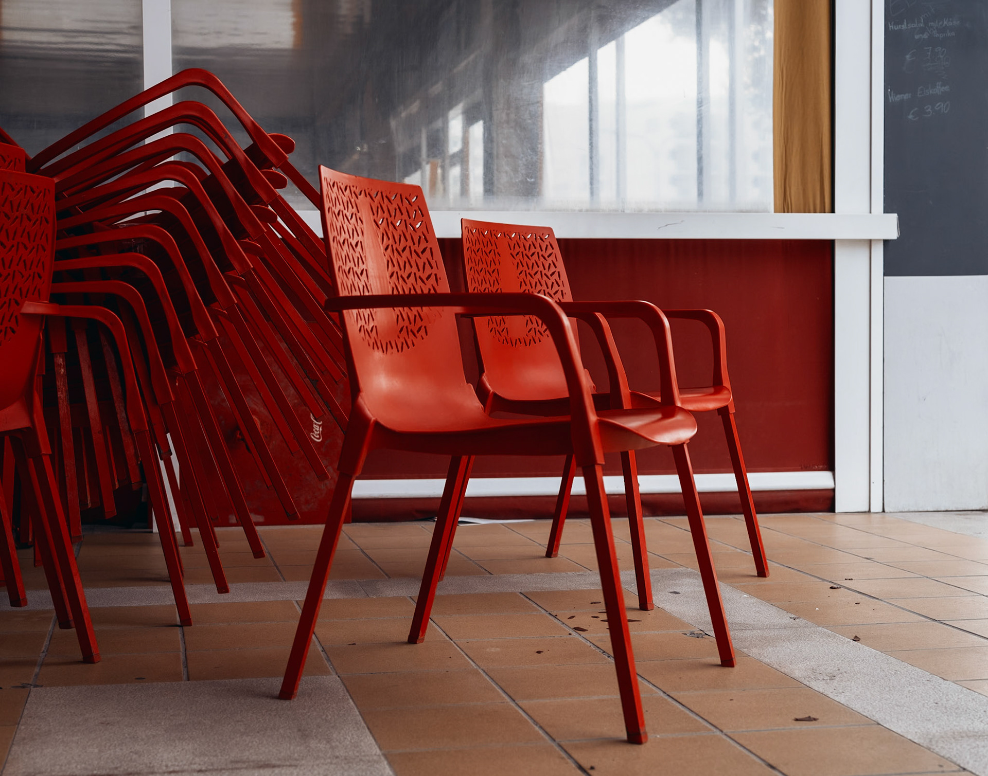 in the hushed quiet of el arenal, the winter season whispers through the empty cafe. red chairs stacked in slumber, a patterned repose of symmetry and stillness. here, the vibrant hustle of summer sleeps, and the chairs wait, silent sentinels of the restful off-season.
