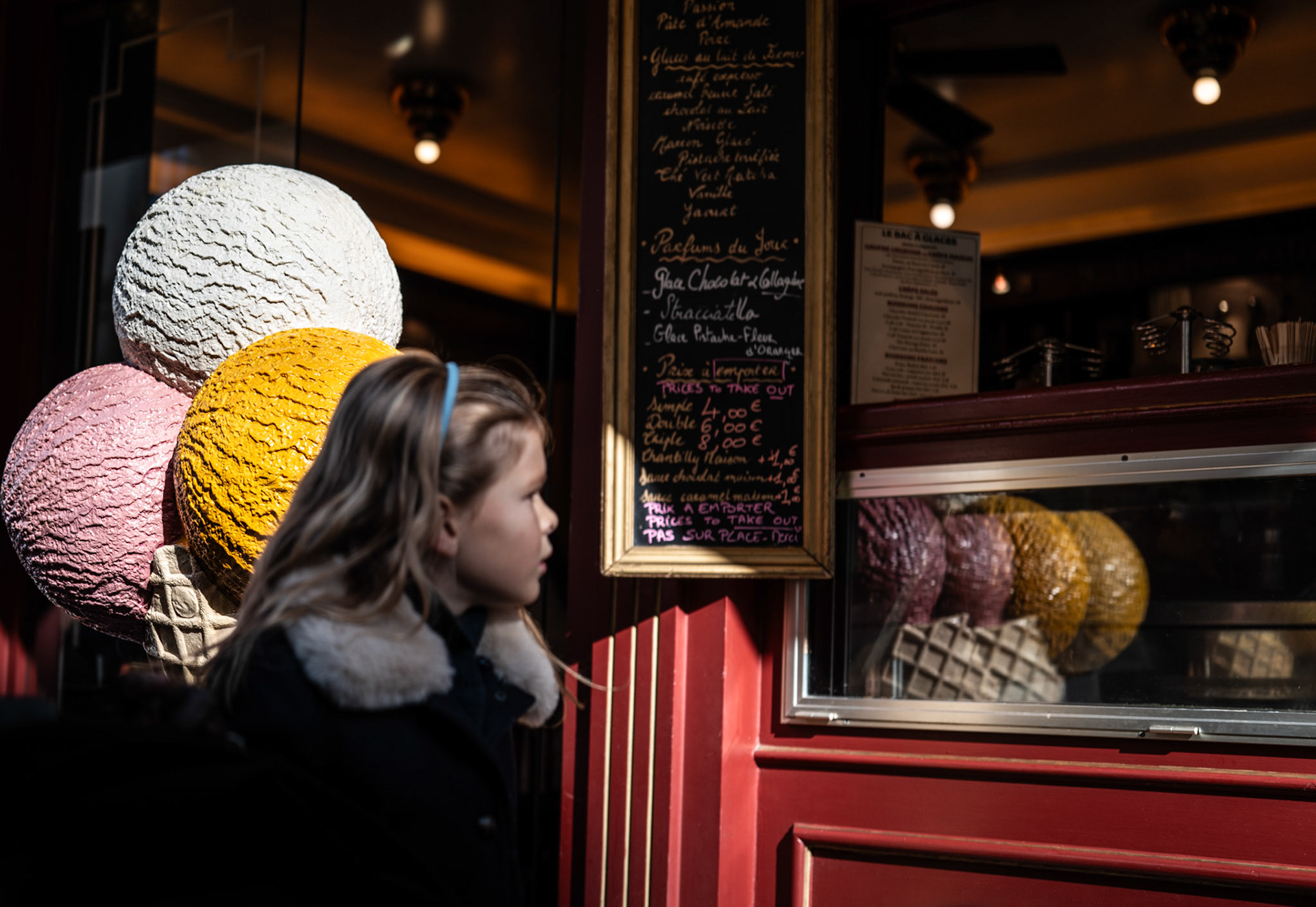 as she strolls down rue du bac, her gaze locks on the colorful ice cream display with a quiet yearning. the vibrant pastel scoops seem almost too perfect, frozen not only in the window but also in time. the moment captures a fleeting sense of desire, a child's fascination with something just beyond reach, blending with the timeless charm of paris. reflections of the bustling street shimmer in the glass, yet her attention remains on the simple joy she dreams of.