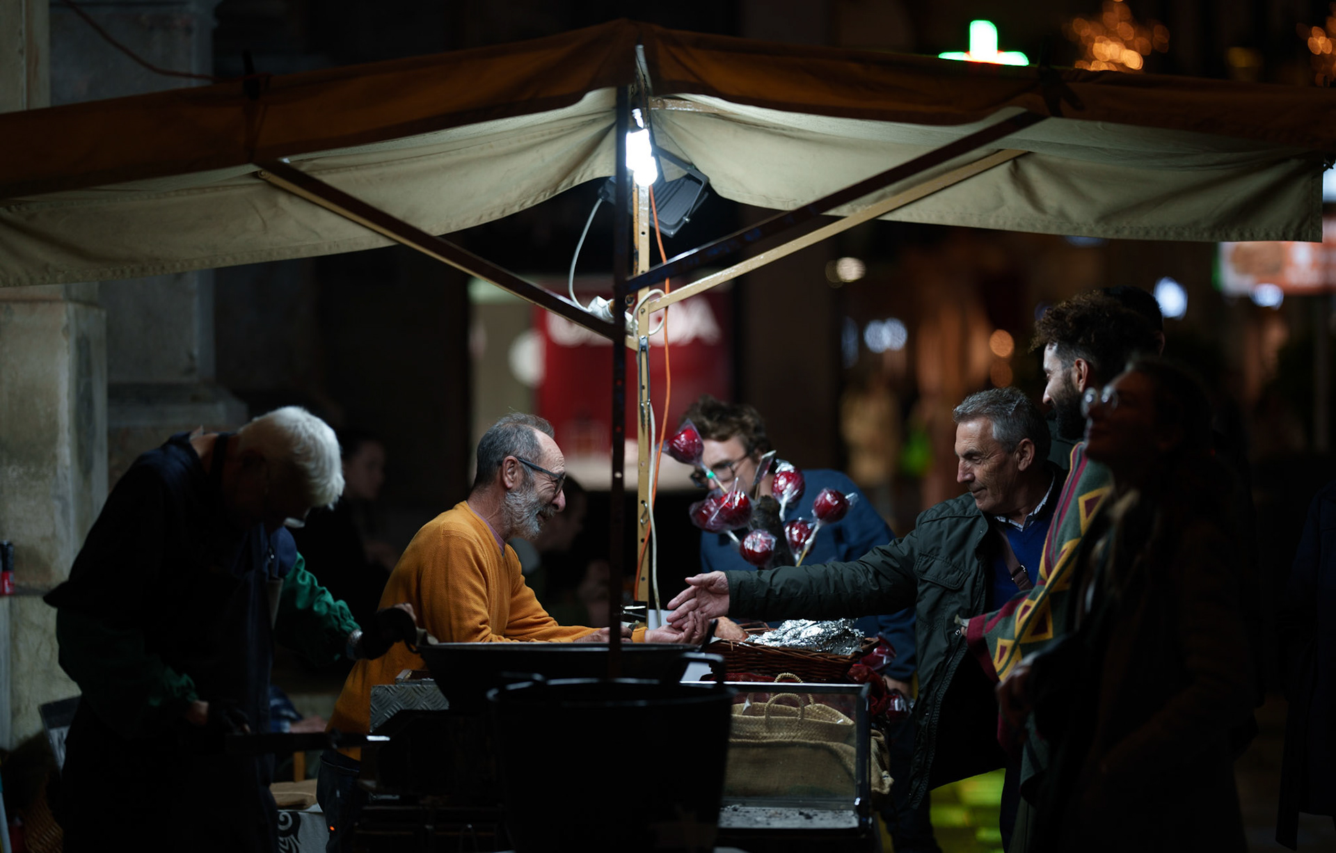 beneath a glowing canopy in the heart of palma de mallorca's bustling city centre, the scent of roasting chestnuts fills the crisp winter night. locals and visitors converge around the warm streetfood vendor, their breaths visible in the air, sharing the simple joy of a traditional winter treat.