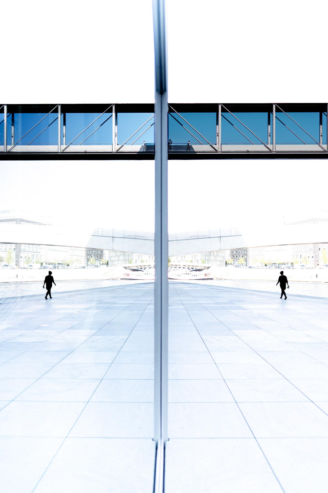 a place where reality blends with reflection, this photo captures the modern lines of the jakob-mierscheid-steg in berlin. framed in blue glass, the bridge seems suspended in both space and time, connecting two sides of the government district. subtle reflections of people walking and cycling create a ghostly overlay, a reminder of the fleeting moments of urban life. while the solid architecture remains fixed, the human presence feels ephemeral, like ripples on the surface of water.
