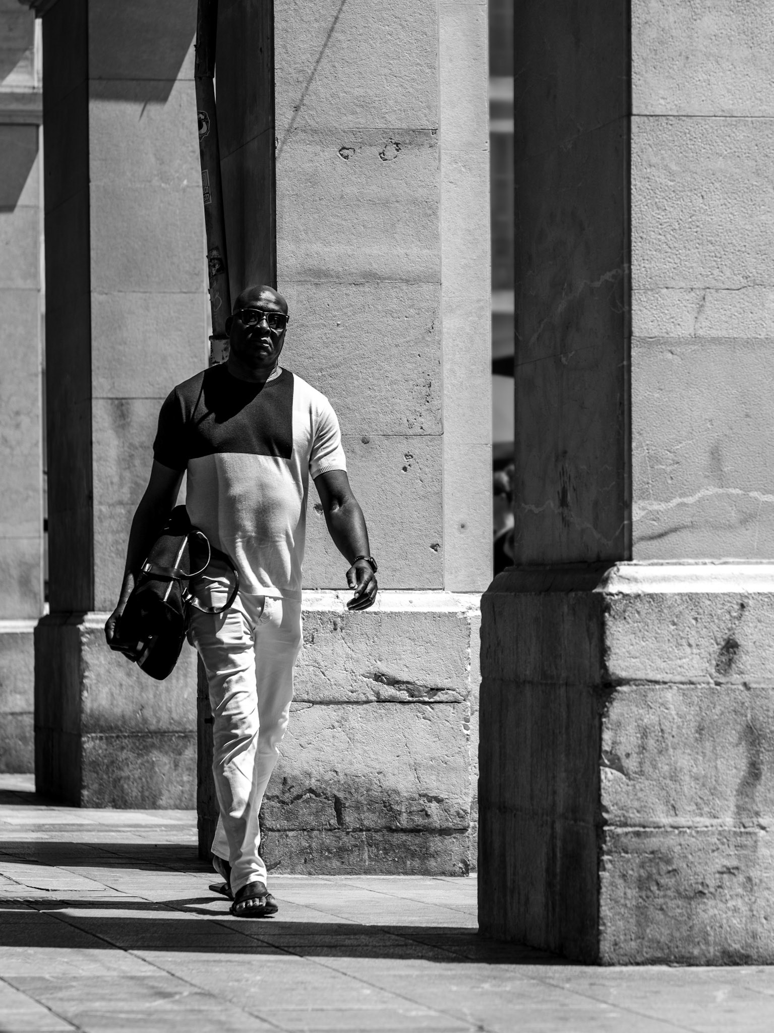 the plaça major in palma de mallorca, an intersection of old and new, comes alive in black and white. a lone figure strides purposefully under the grand arches, casting long shadows that dance with the sunlight. the interplay of light and dark reveals the textures of ancient stone and the quiet determination in his gait. this image captures a moment in time, a testament to the enduring spirit that walks through the corridors of history.