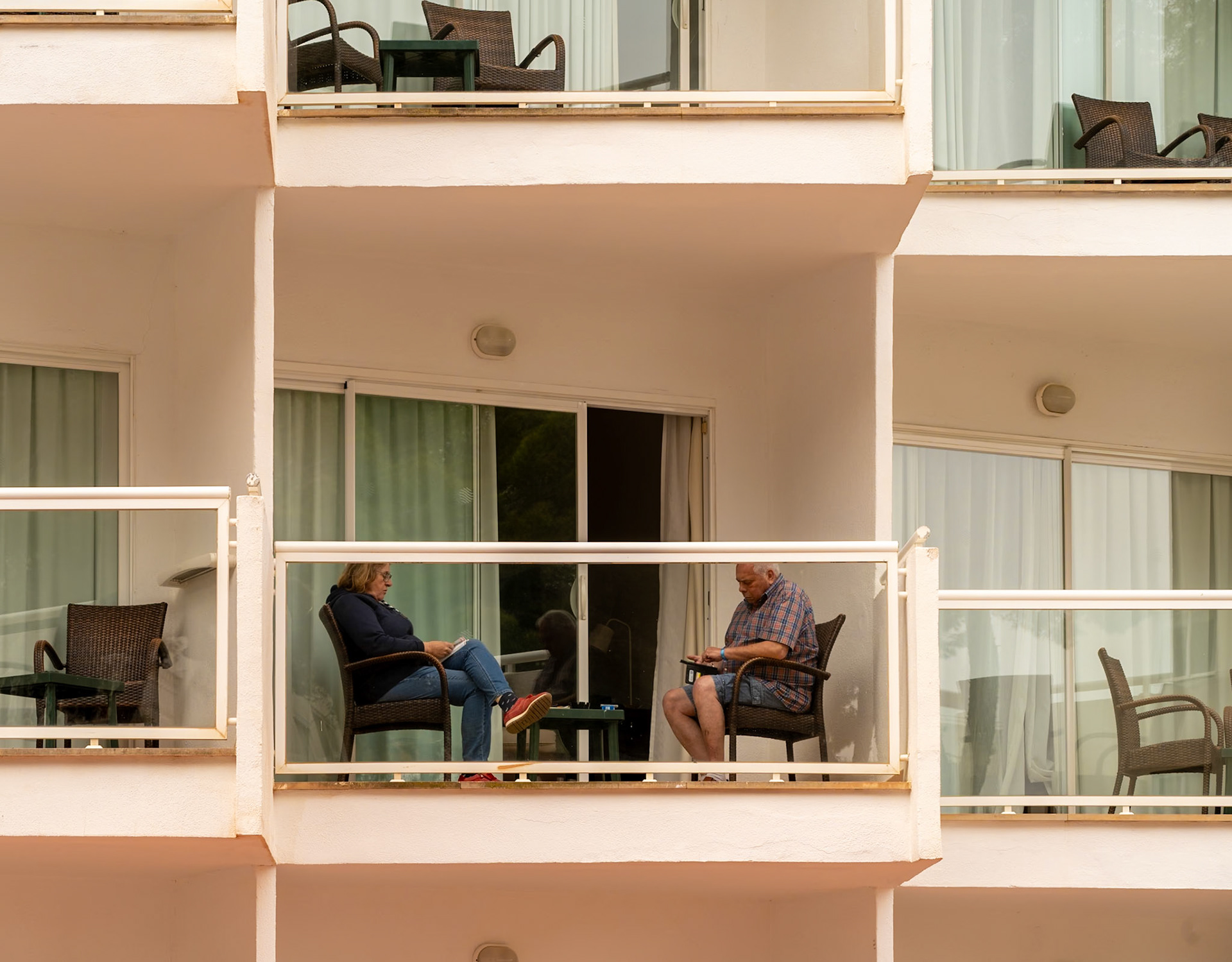 in magaluf, the quiet narrative of "on the balcony" unfolds, where two figures engage in a silent exchange. seated across from one another, their posture speaks volumes – one leans forward, perhaps mid-conversation or lost in a book, while the other reclines, absorbed in thought or simply savoring the stillness. it's a scene of everyday life, yet it captures the essence of human connection without a word being uttered. the balconies, parallel stages of individual stories, hold a mirror to the tranquil pace of life, a reminder of the comfort found in one's own space, yet in subtle communion with another.