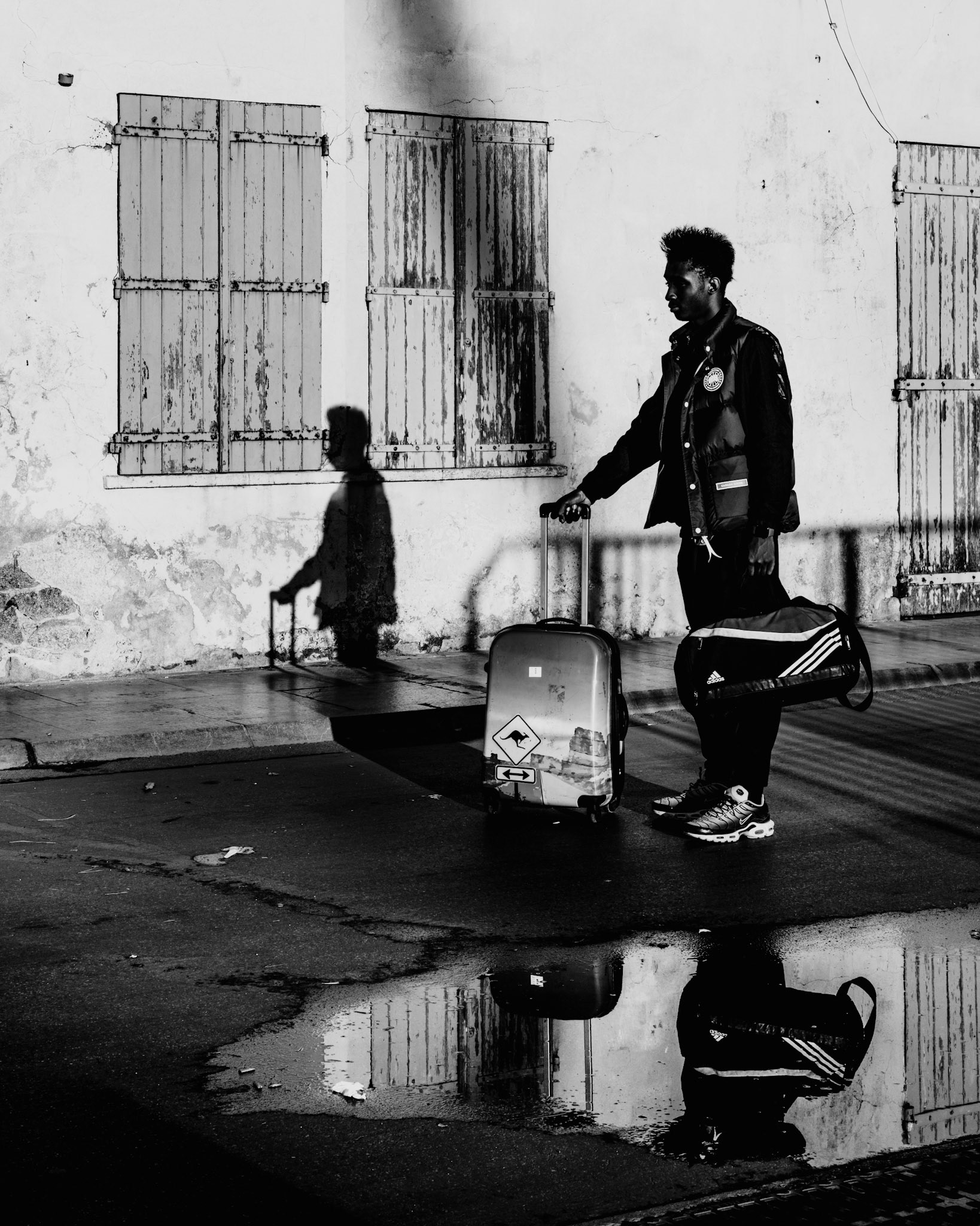 in the serene early hours of Saint-Tropez, the world seems to pause in quiet contemplation. a lone traveler, bathed in the soft morning light, pulls his vibrant blue suitcase past weathered shutters and puddle reflections, each step echoing the promise of new destinations. the rich textures of the old wall contrast with the fresh anticipation in the traveler’s stride, capturing a poignant moment of transition and the timeless beauty of this historic port town.