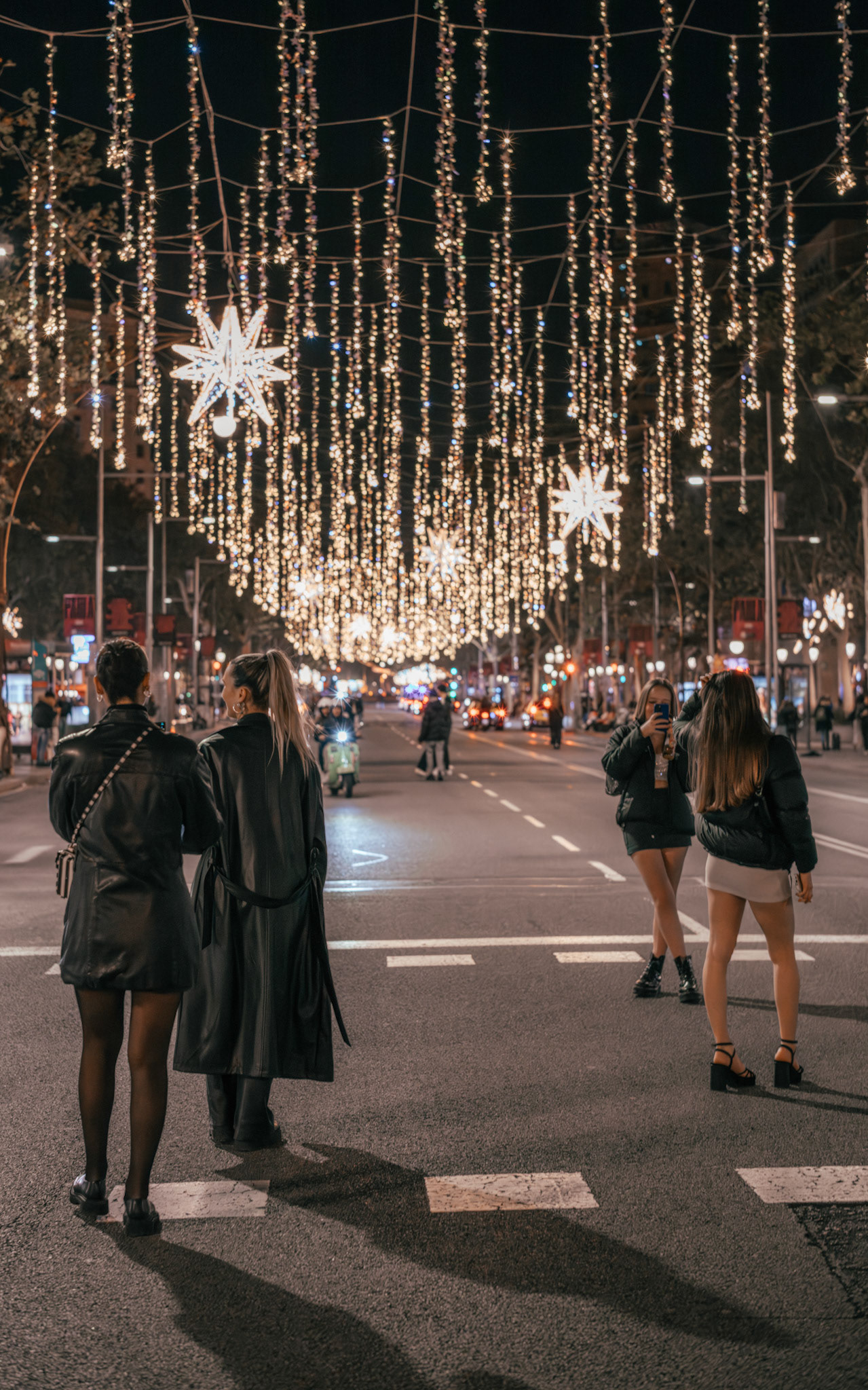 captured in the winter in barcelona, the city comes alive at night with streets adorned in sparkling lights. friends gather, basking in the warm glow of festive decorations, their laughter mingling with the ambiance of the season. the night, filled with stylish urban dwellers, becomes a canvas of holiday cheer.