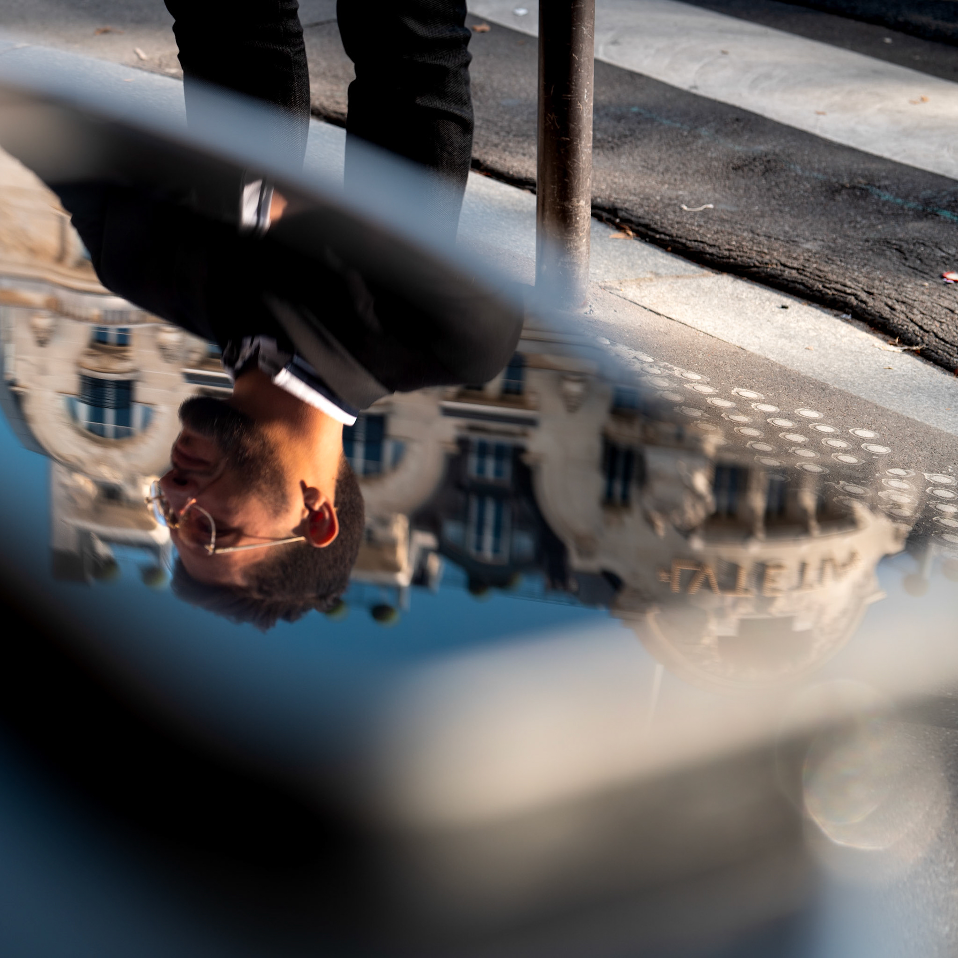 n the fleeting chaos of the city, this moment caught my eye. a man, sharply dressed, walking past without realizing his reflection was captured in a thin film of water on the street. the soft blur of the surroundings blends with the crispness of the reflection, creating a visual contrast that speaks to the tension between movement and stillness. the architecture behind him, echoing the grand facades of paris, merges seamlessly into his mirrored image, making it unclear where the man ends and the city begins. it’s a brief, poetic moment of connection between man and metropolis.
